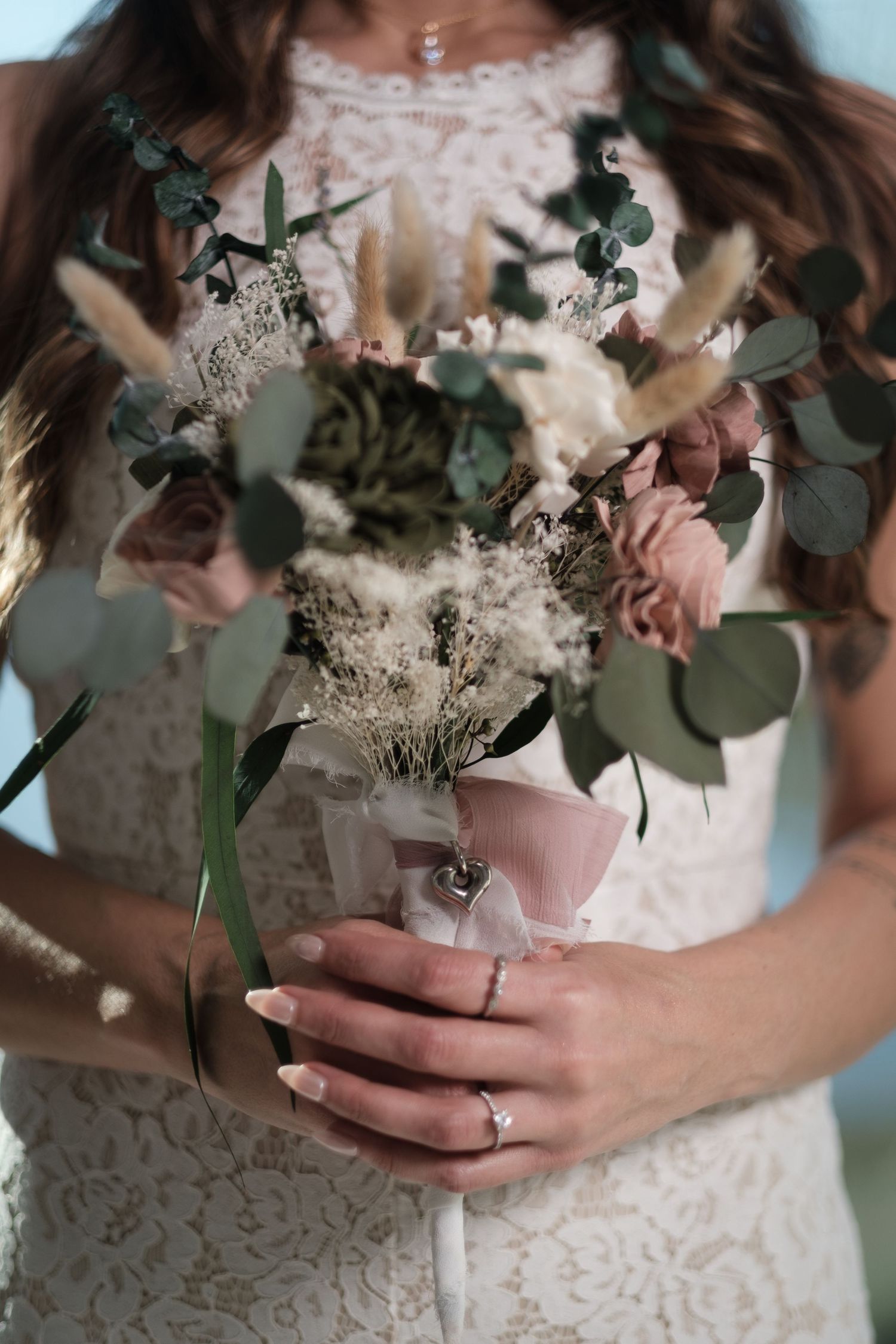 Close-up view of a bridal bouquet with white flowers and eucalyptus leaves held against a lace wedding dress.