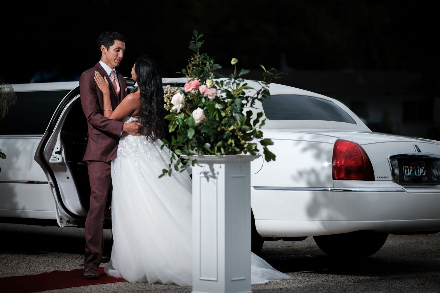 Artistic black and white wedding photo with classic car silhouette in background.