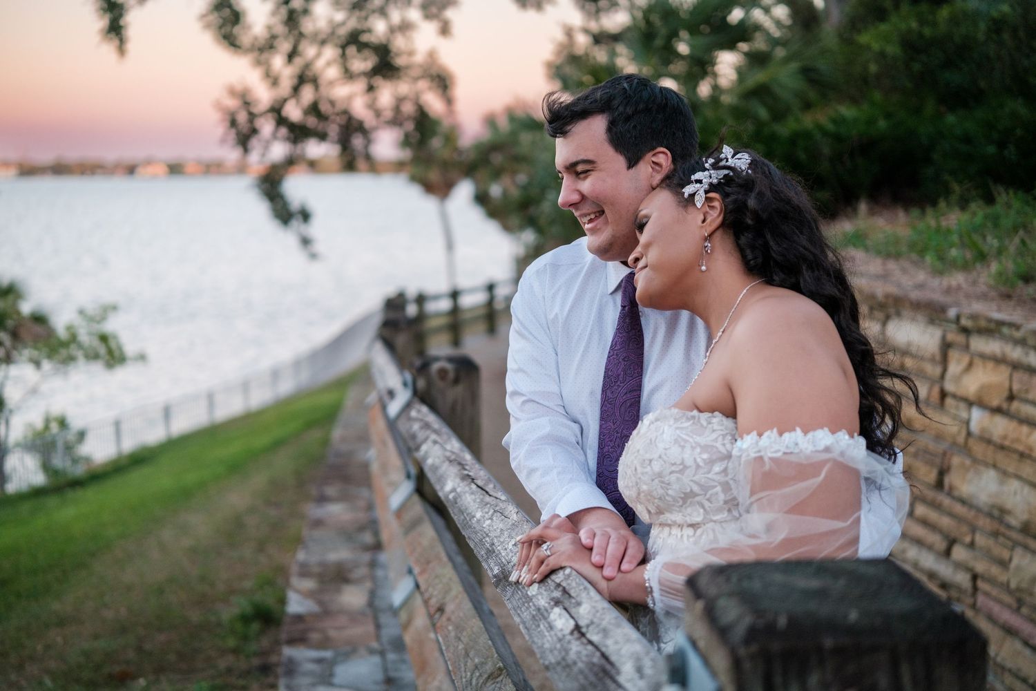A couple shares romantic moments at sunset along a stone wall during their wedding photo session.