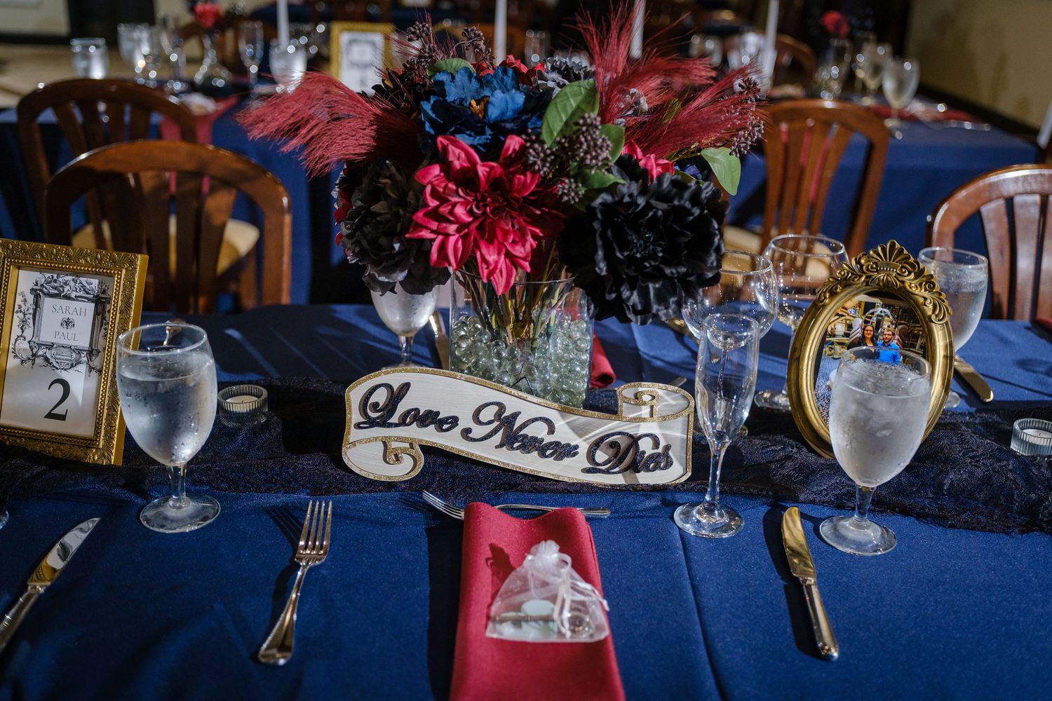Wedding reception table settings with navy blue tablecloths, pink floral centerpieces, and elegant glassware.