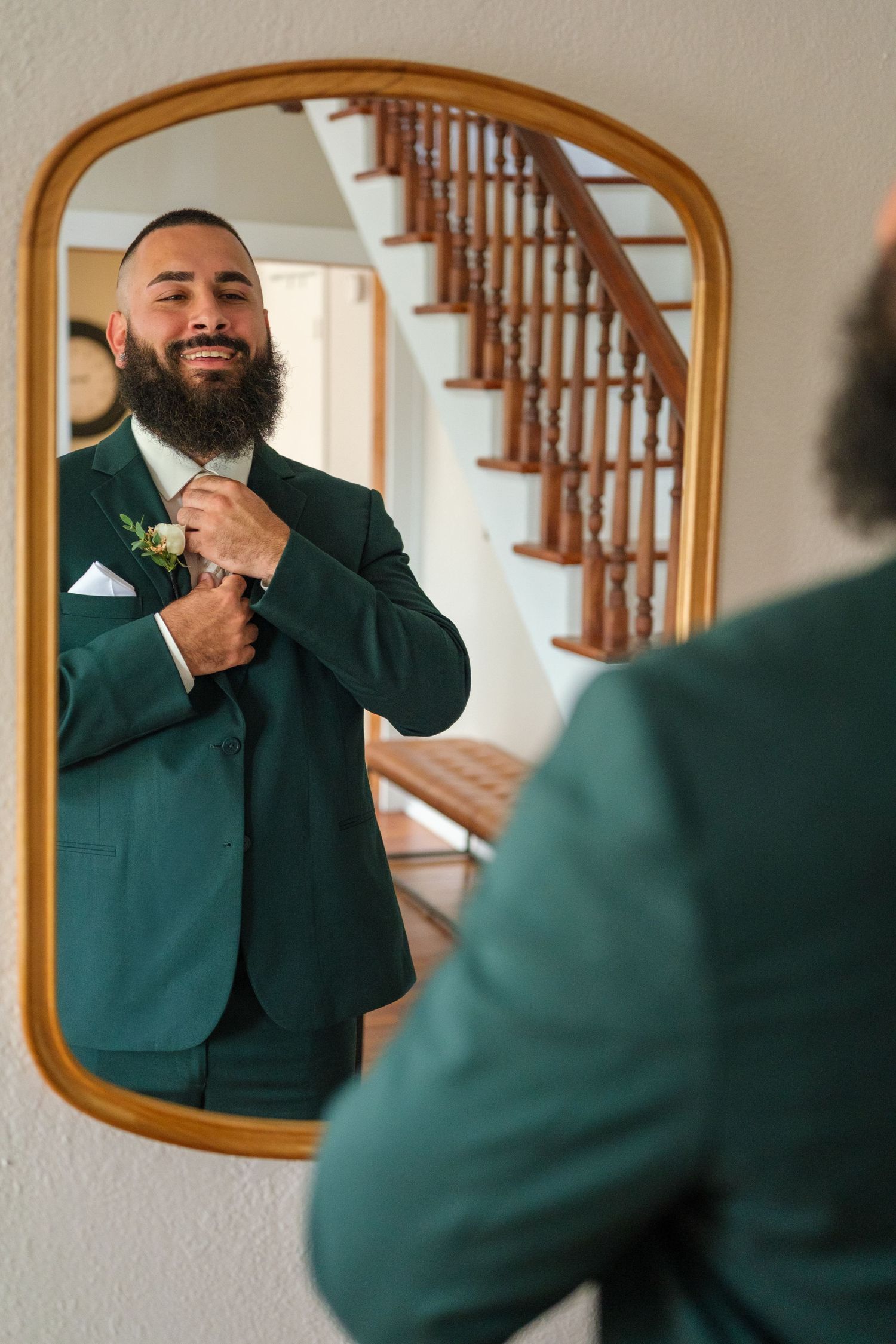 A person wearing a green suit adjusts their tie while smiling in front of a series of arched mirrors.