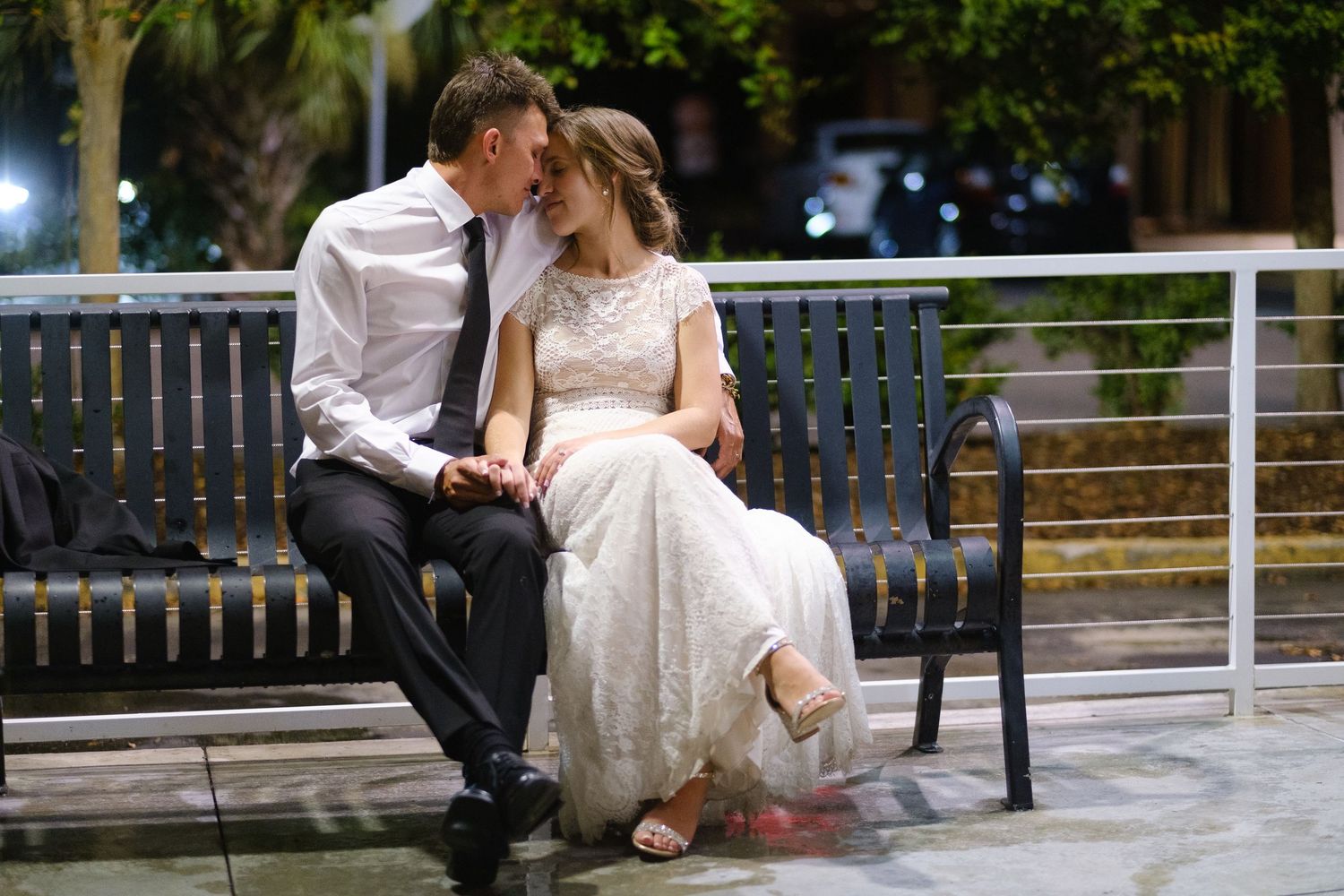 Bride and groom sit together on a park bench in wedding attire sharing an intimate moment.