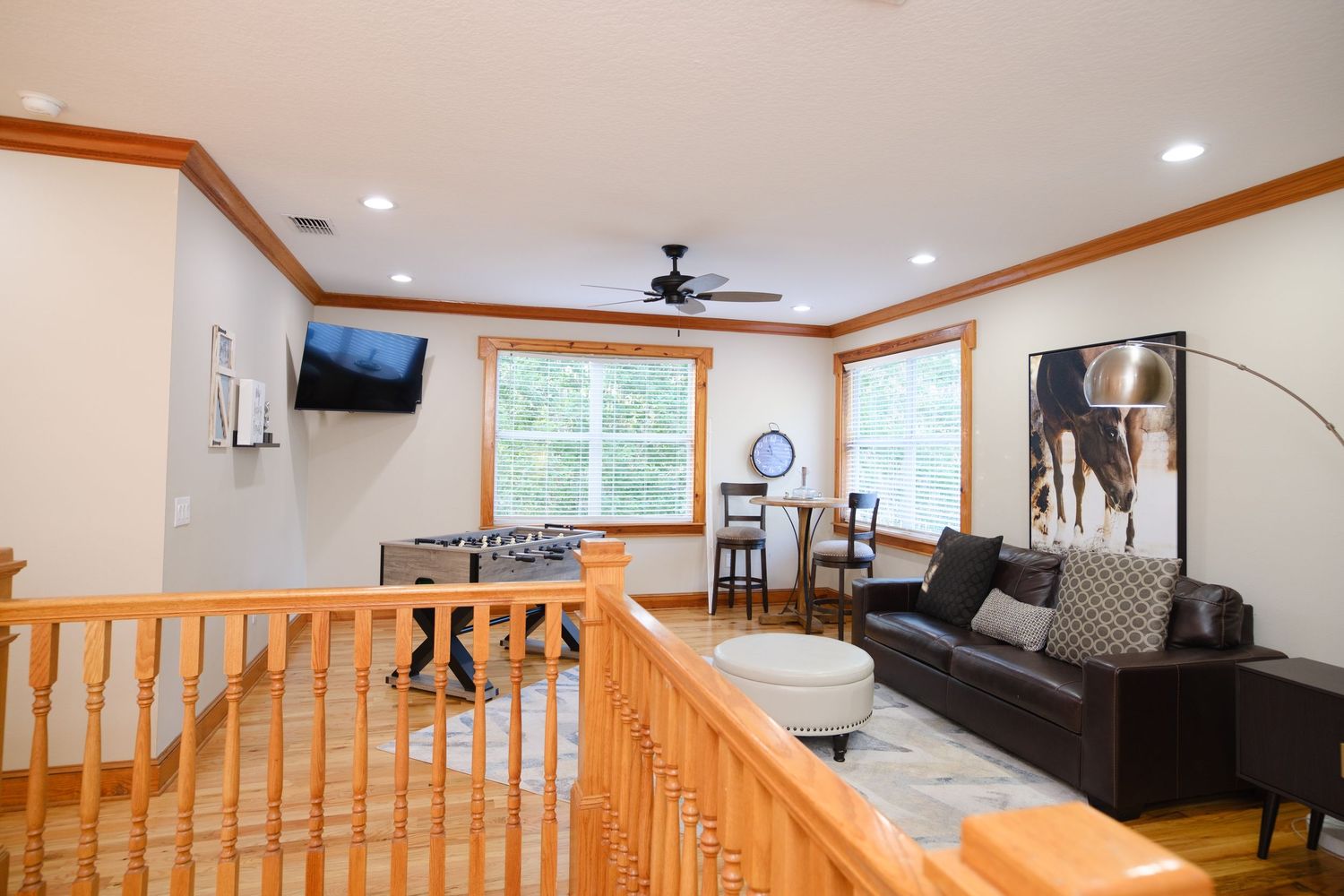 Open concept living area with leather sectional and wooden railings featuring large windows and crown molding.