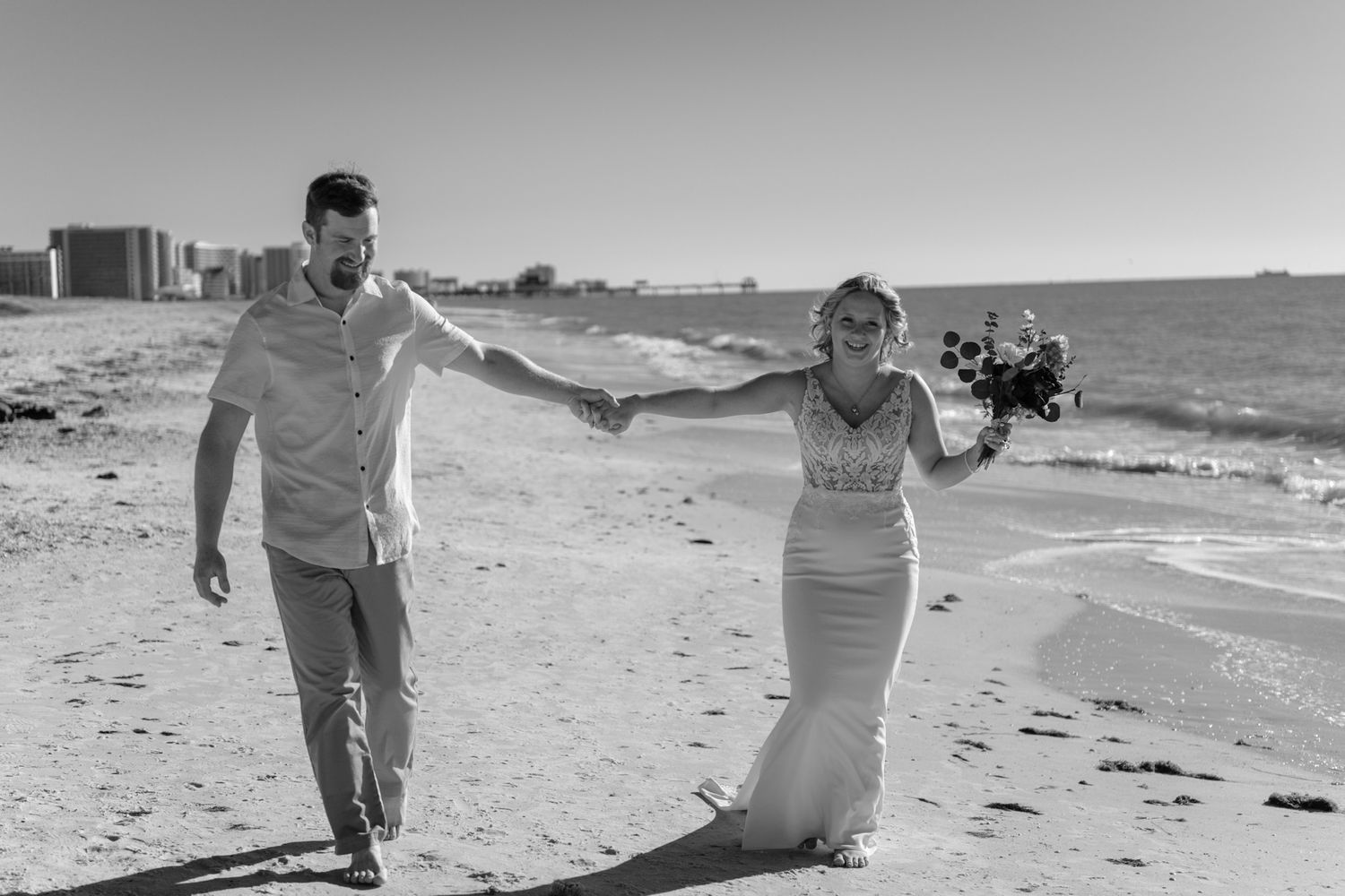 Black and white photo of a couple walking together on a beach during their wedding day.