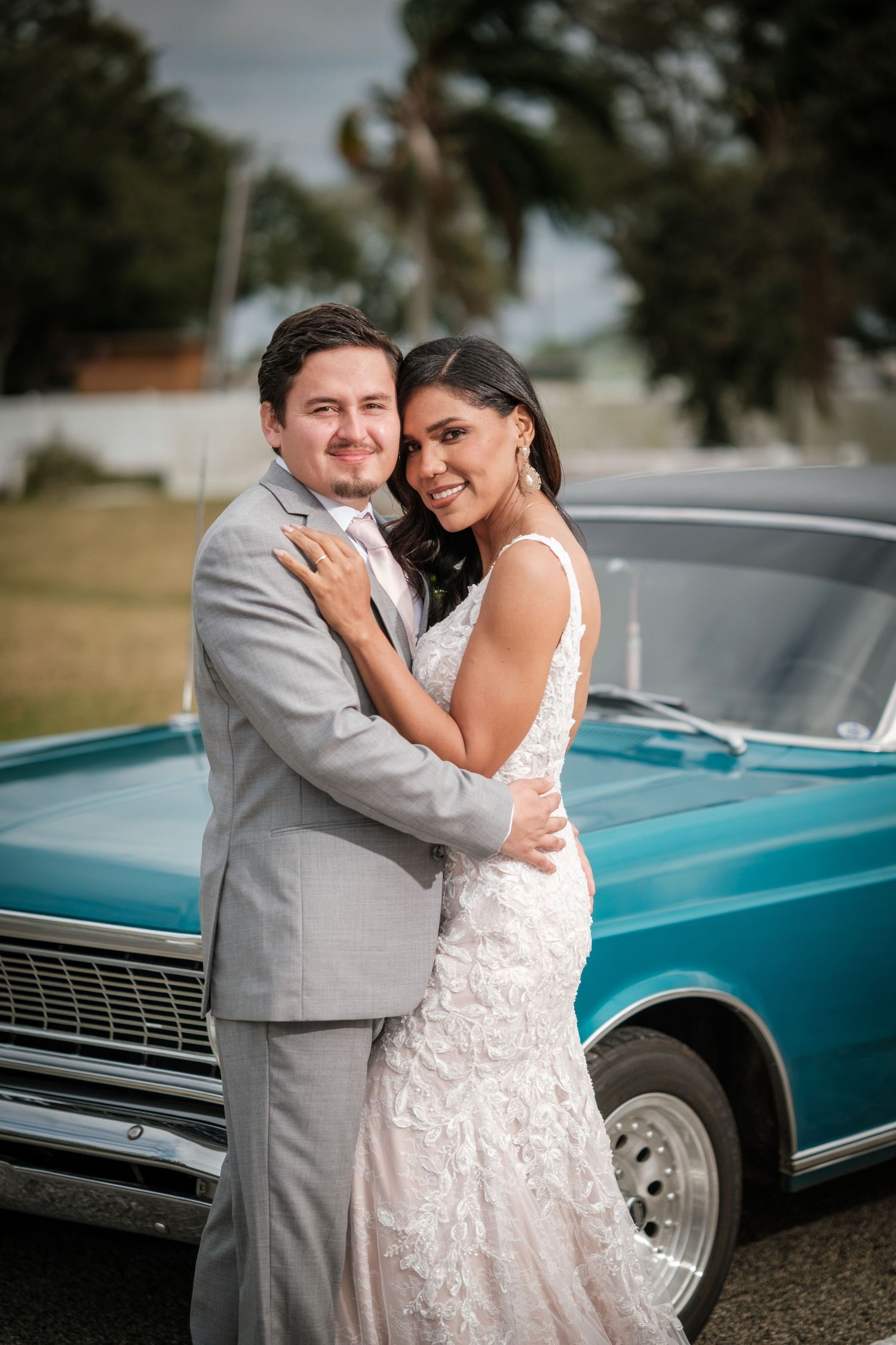 Wedding couple poses romantically next to a vintage turquoise car on their special day.
