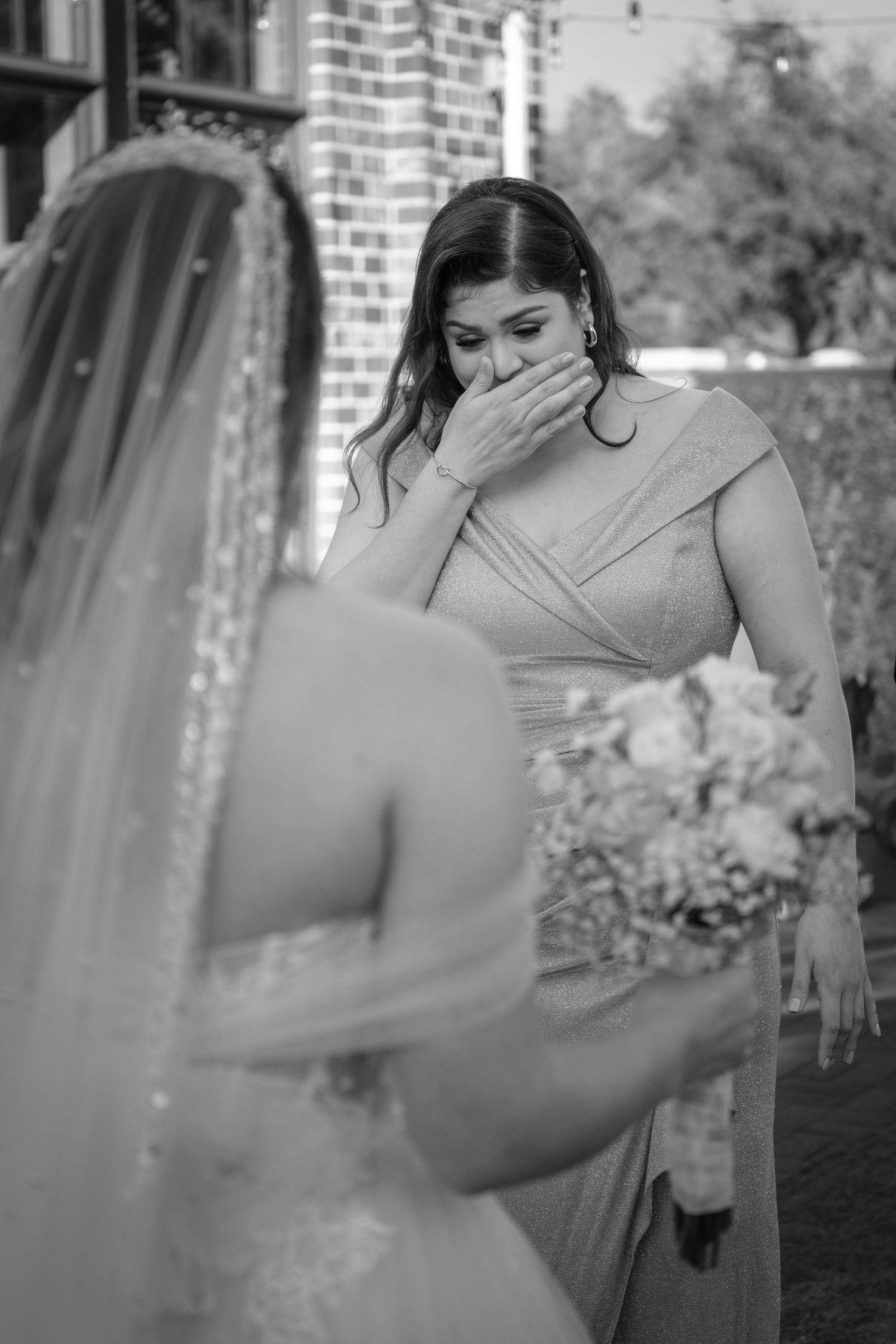 Black and white photo of emotional bridesmaid covering her mouth in tears during a wedding day first look ceremony.