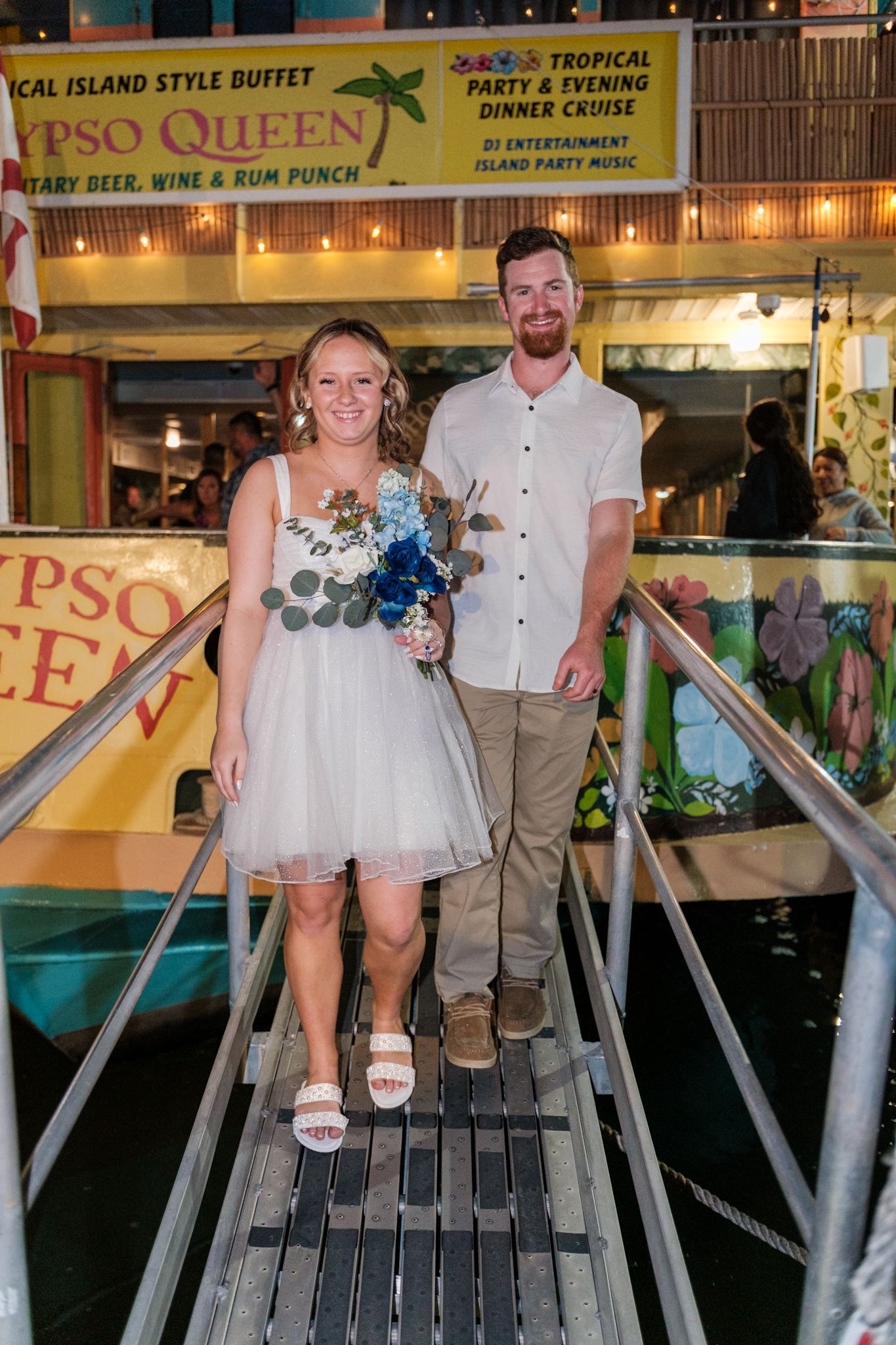 A couple poses on a walkway in front of a tropical restaurant sign.
