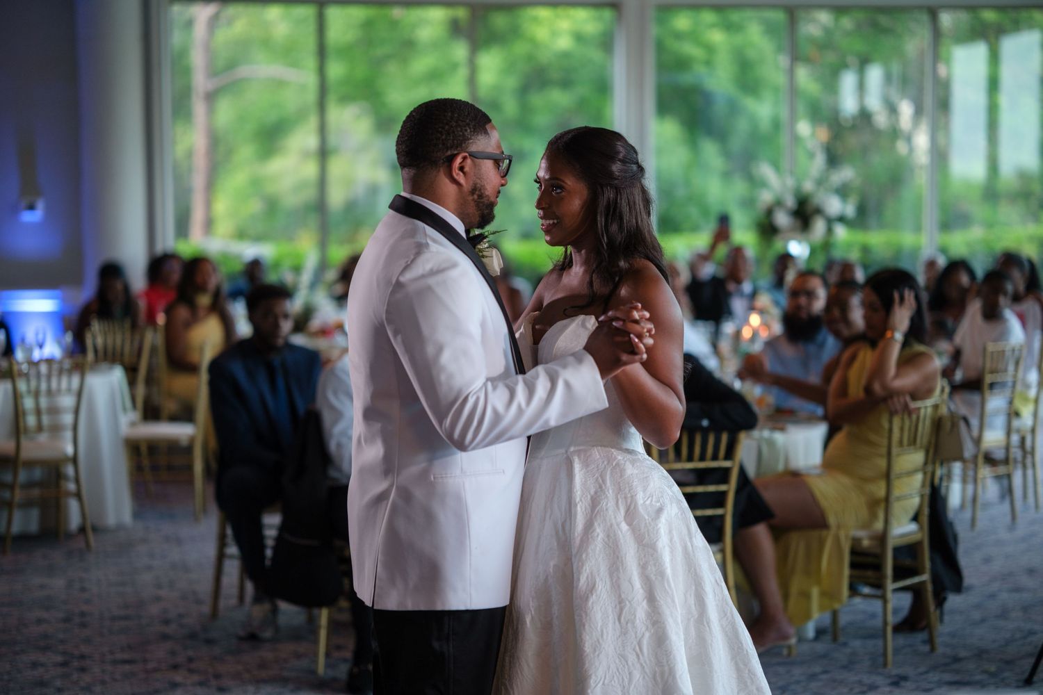 Bride and groom share their first dance at an elegant wedding reception with guests seated in the background.