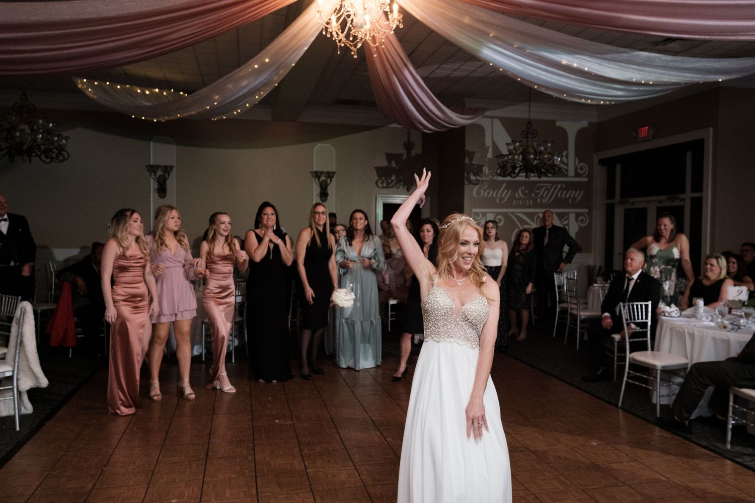 Wedding guests dance and celebrate on a dimly lit dance floor under draped fabric decorations at an evening reception.