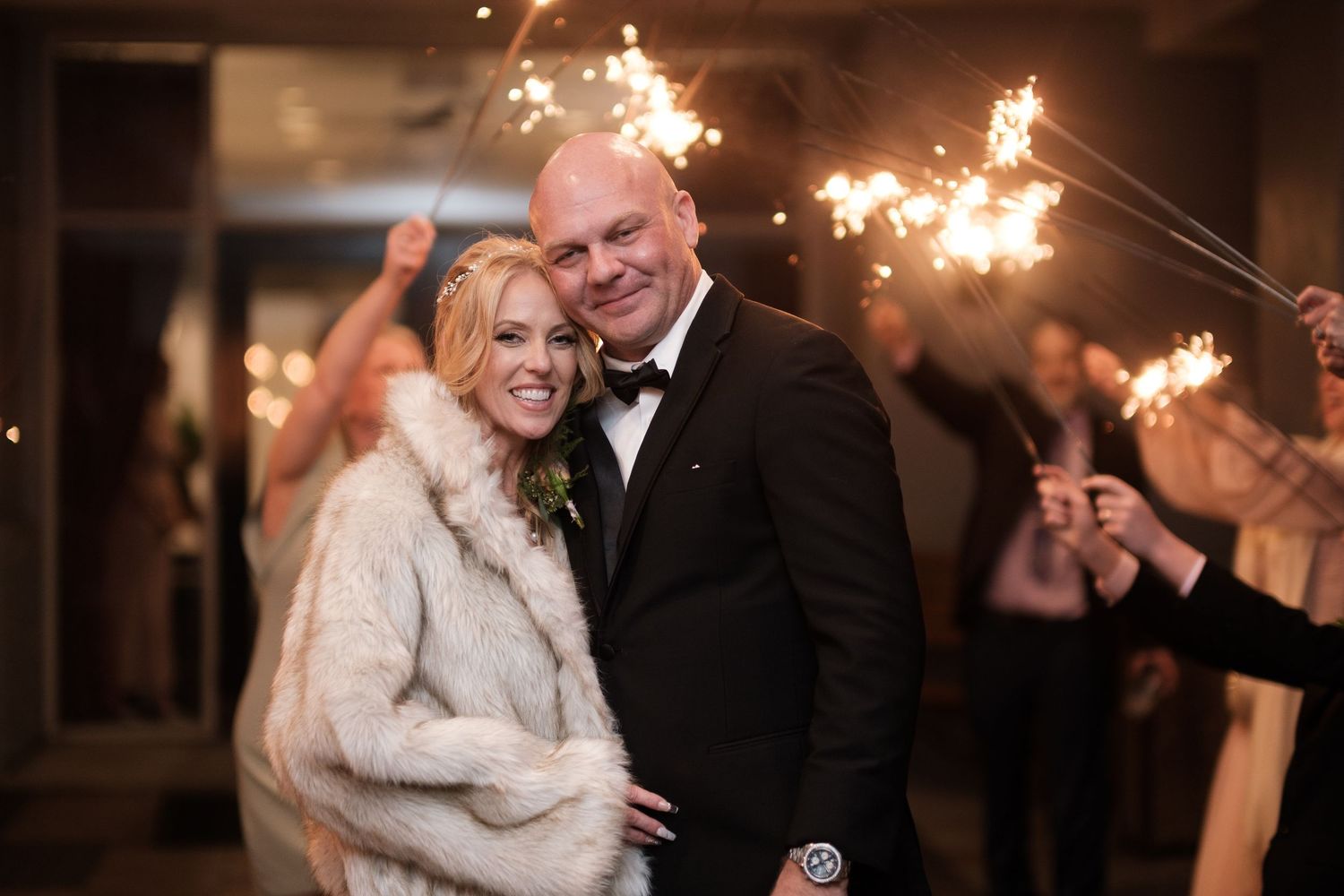 A couple shares a romantic moment together during their winter wedding celebration with sparklers glowing in the background.