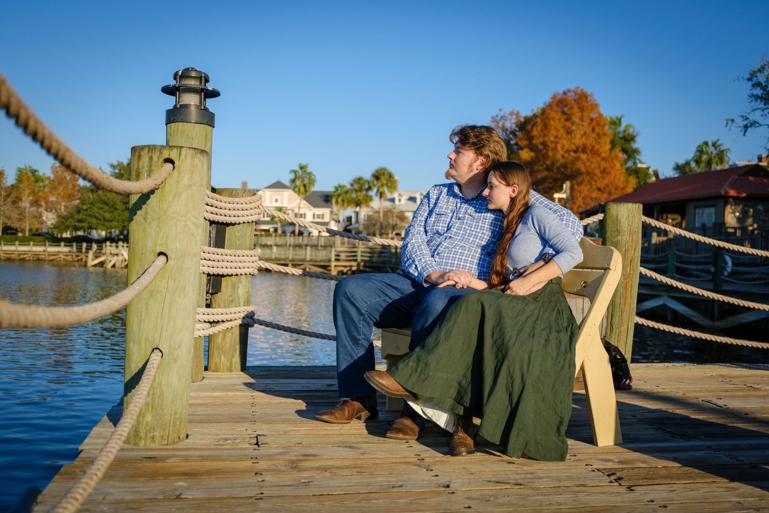 Couple sitting together on a wooden pier by the water, sharing a romantic moment at golden hour.