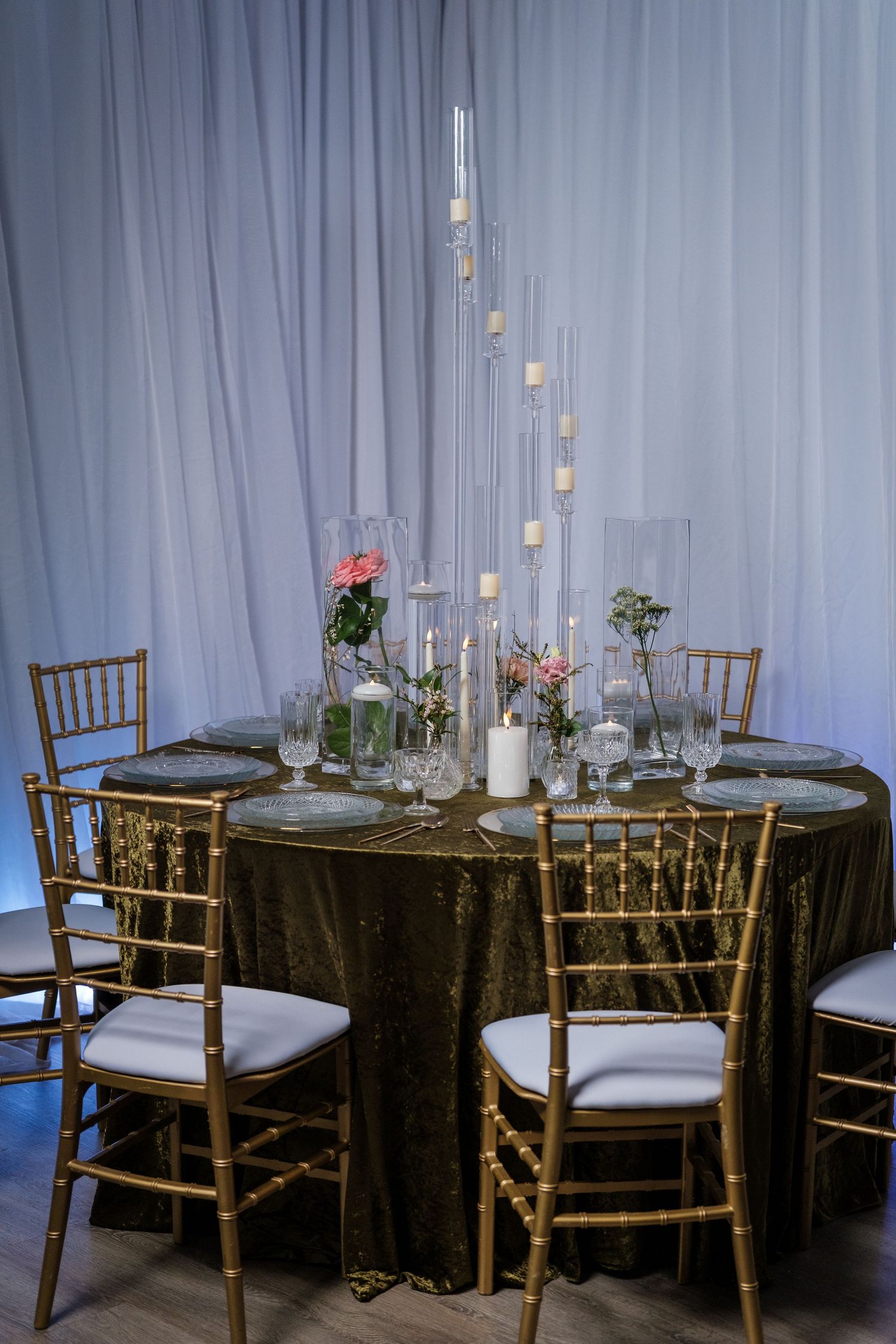 Wedding reception setup with gold chiavari chairs and dark tablecloths under soft lighting.