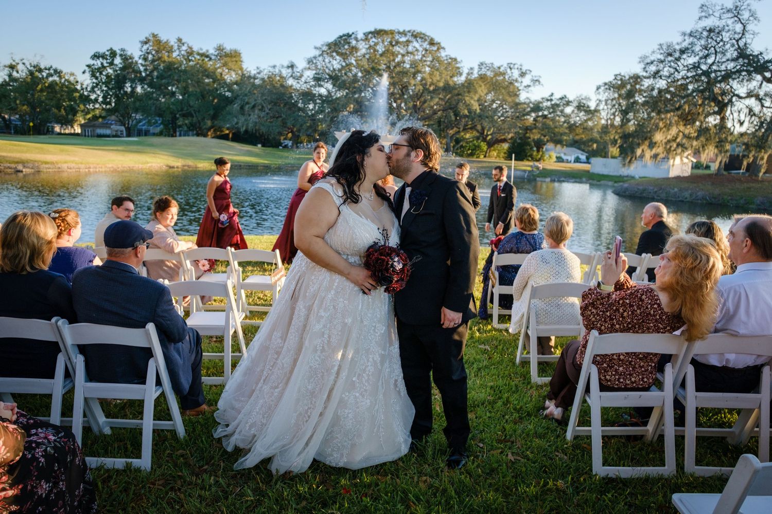 Outdoor wedding ceremony setup with white chairs arranged in rows on a grassy lawn at sunset.