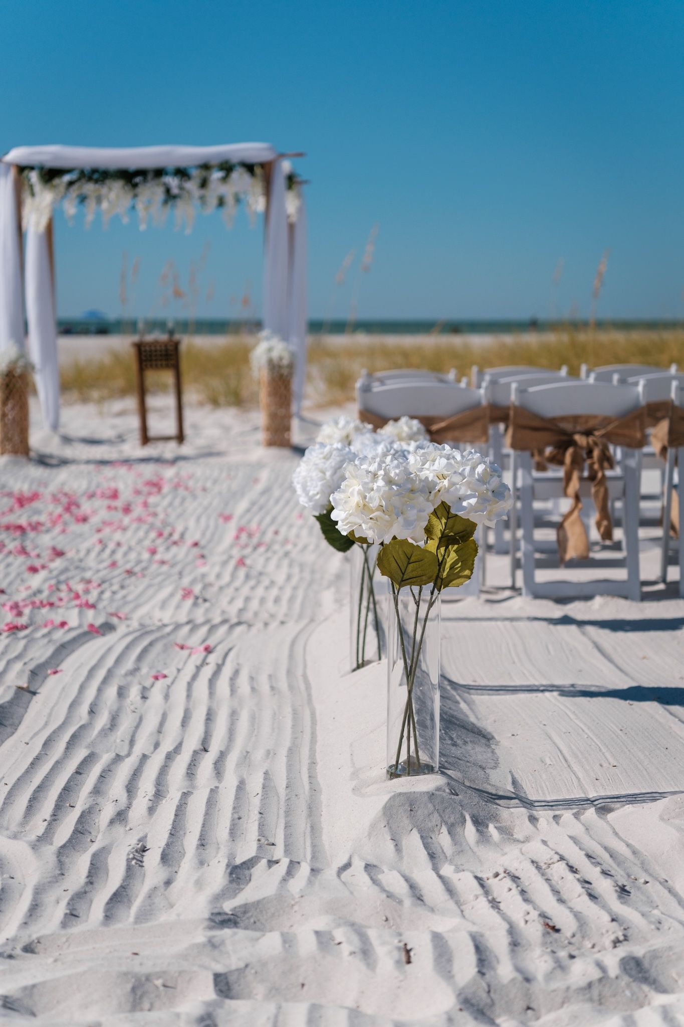 Elegant beach wedding aisle lined with scattered pink petals and white floral arrangements.