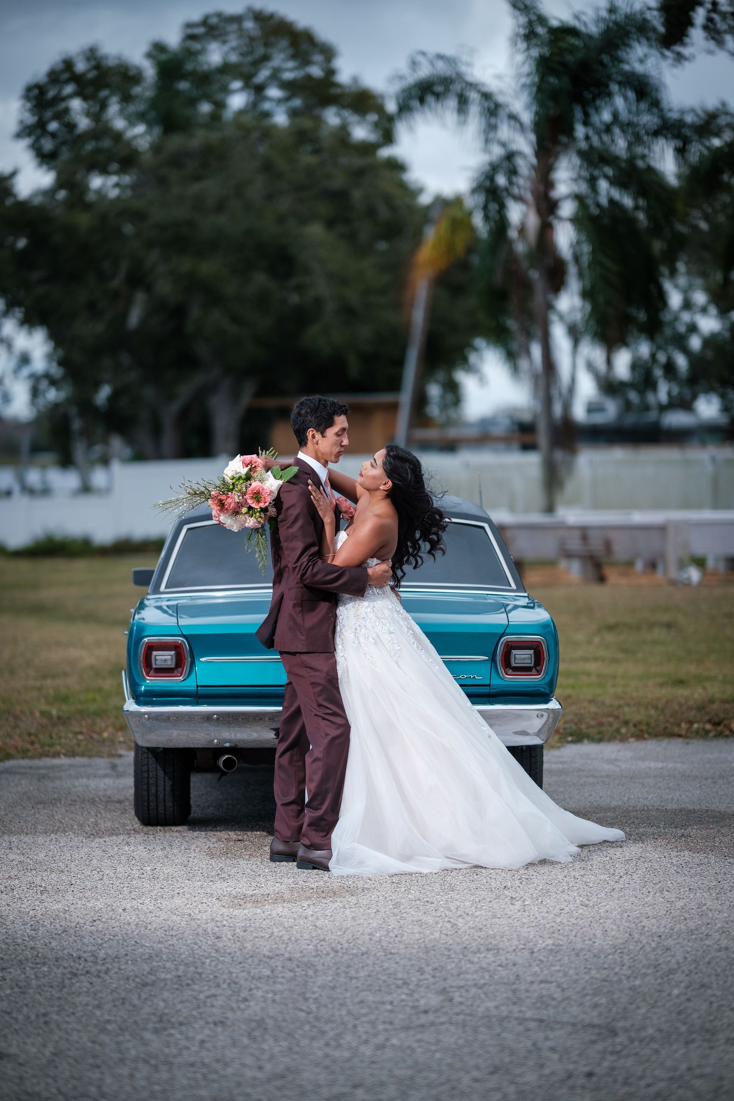 Newlyweds share an intimate moment against a vintage turquoise truck with trees in the background.
