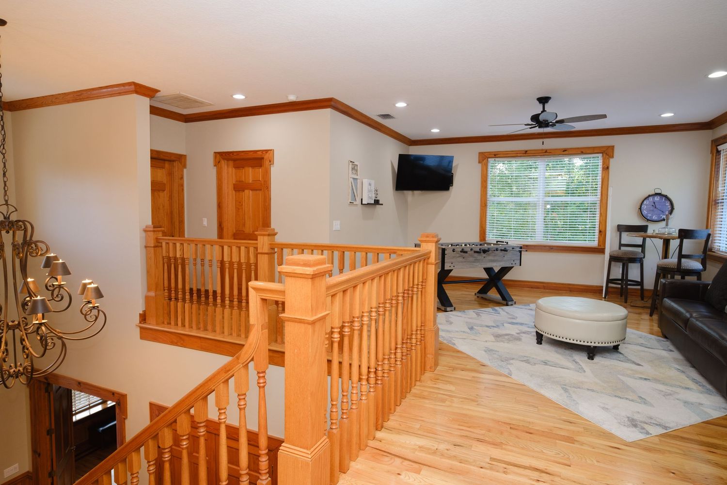 Upstairs landing area with honey oak staircase railing, hardwood floors and elegant chandelier in modern home interior.