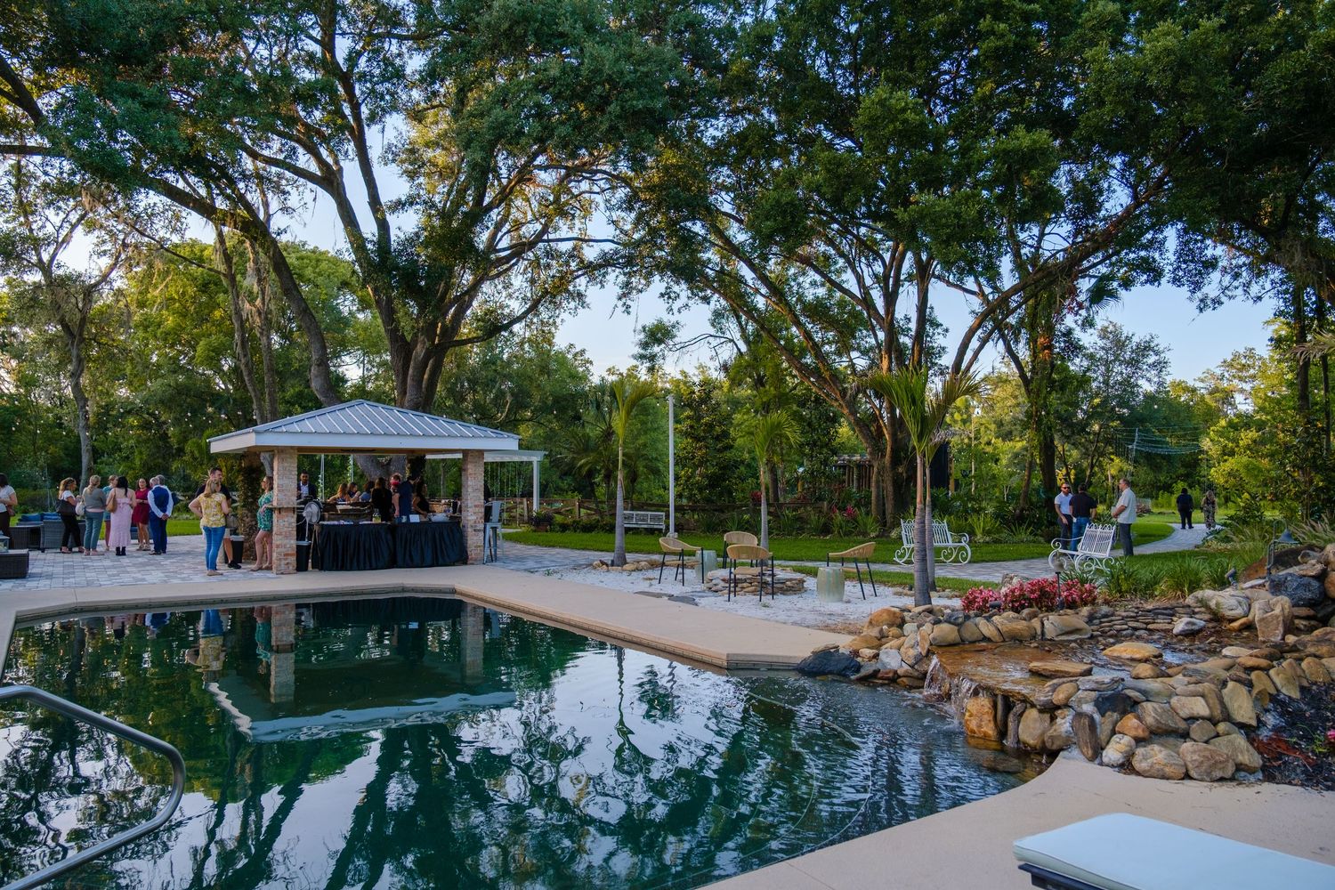 A gazebo overlooks a tranquil reflecting pool surrounded by trees and landscaping rocks in a scenic park setting.