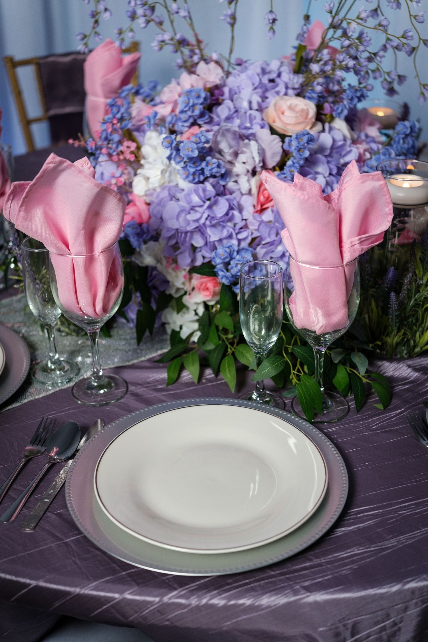 Elegant table setting with pink roses and purple flowers on a dark tablecloth with white plates.