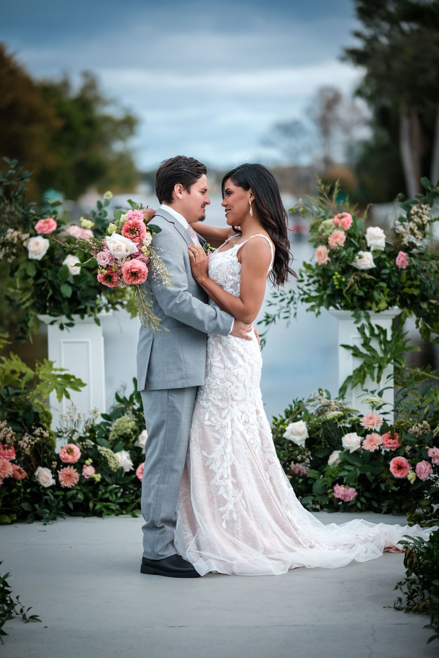 A bride and groom dance together in a romantic garden setting with pink roses and greenery.