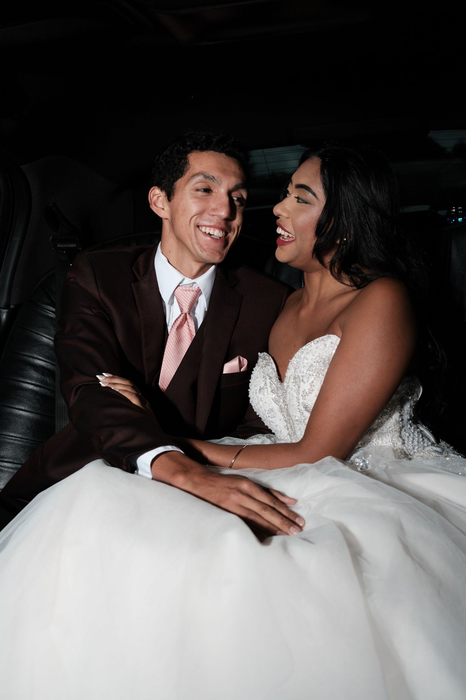 Newlyweds share intimate moments and laughter while seated in a luxurious car interior.