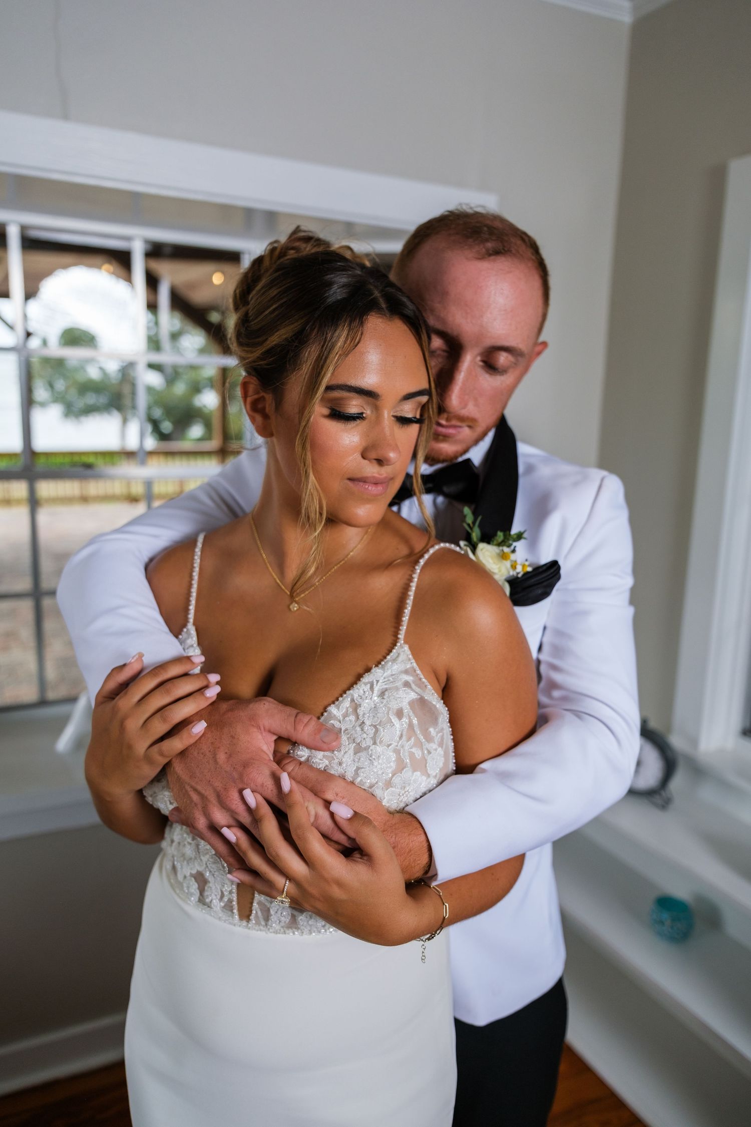 A romantic wedding moment with a couple embracing in an elegant white dress and suit in a bright indoor setting.