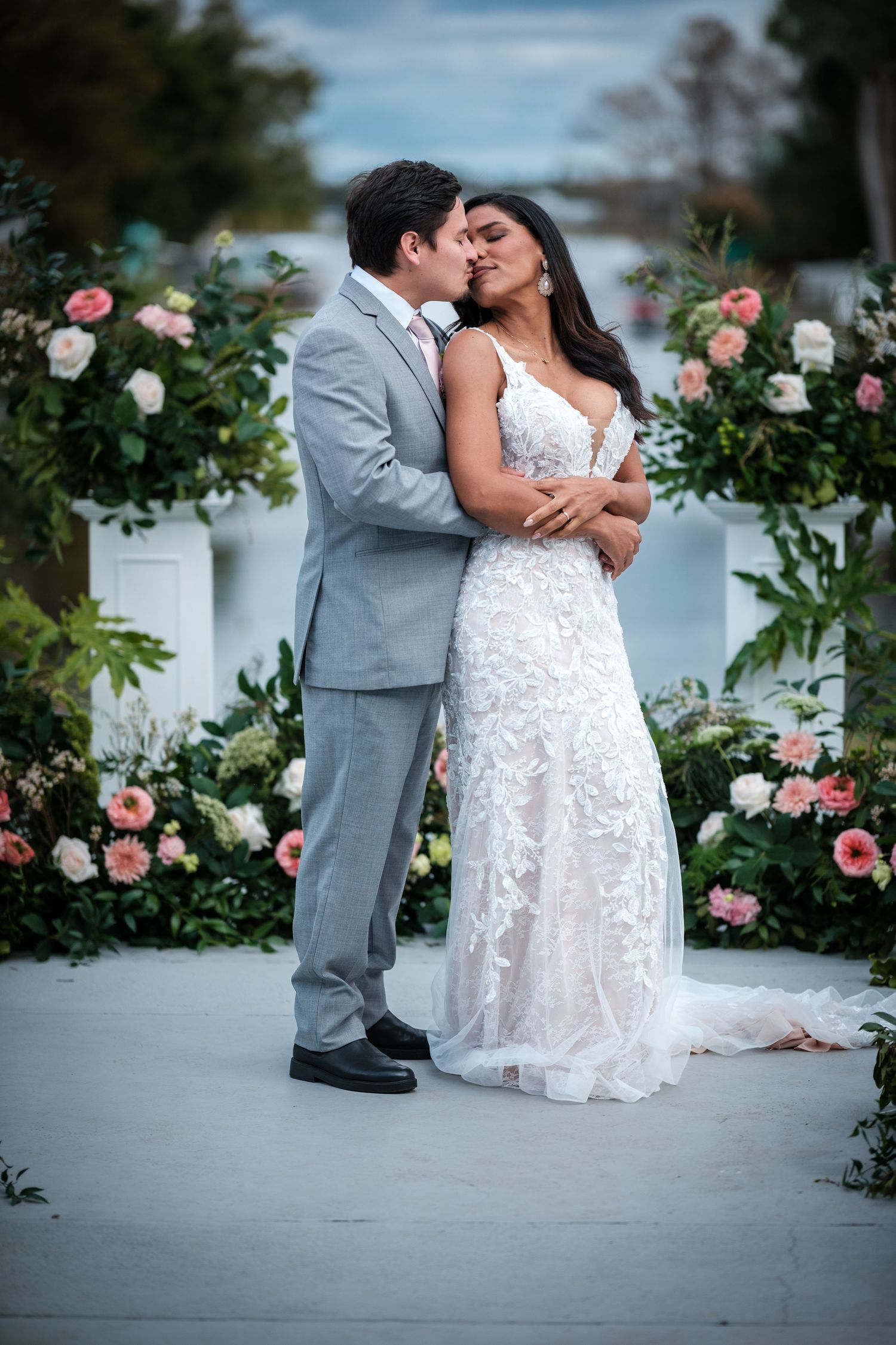 Romantic wedding couple poses in front of blooming rose bushes in a garden setting.