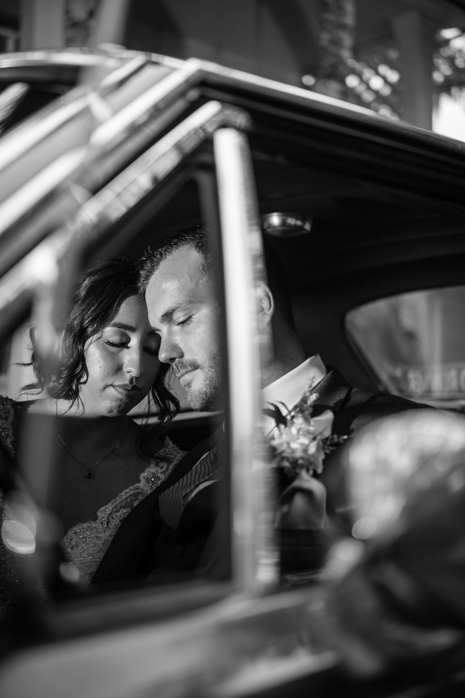 A tender moment captured in black and white as newlyweds share an intimate moment in the back of their car.