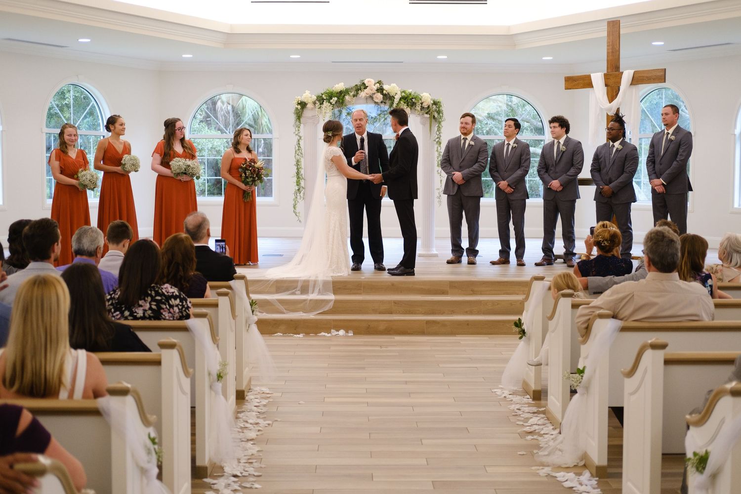 A series of wedding ceremony photos showing a church interior with floral decorations and guests standing in formal attire.