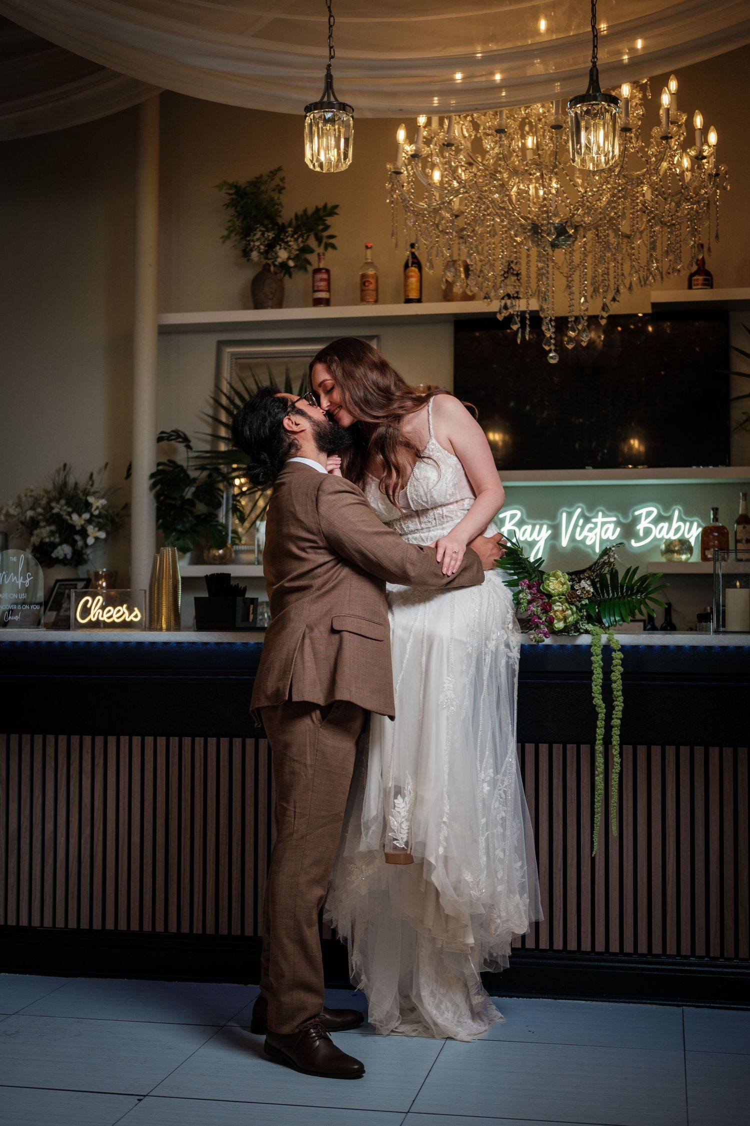 Bride and groom share first kiss at elegant bar venue with chandelier lighting.