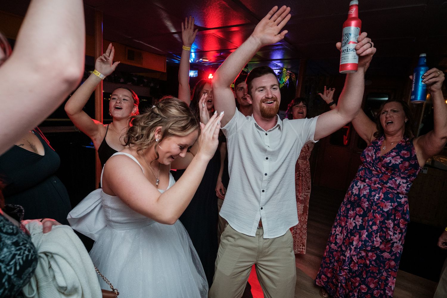 Lively dance floor scene at wedding reception with guests celebrating under dim lighting.