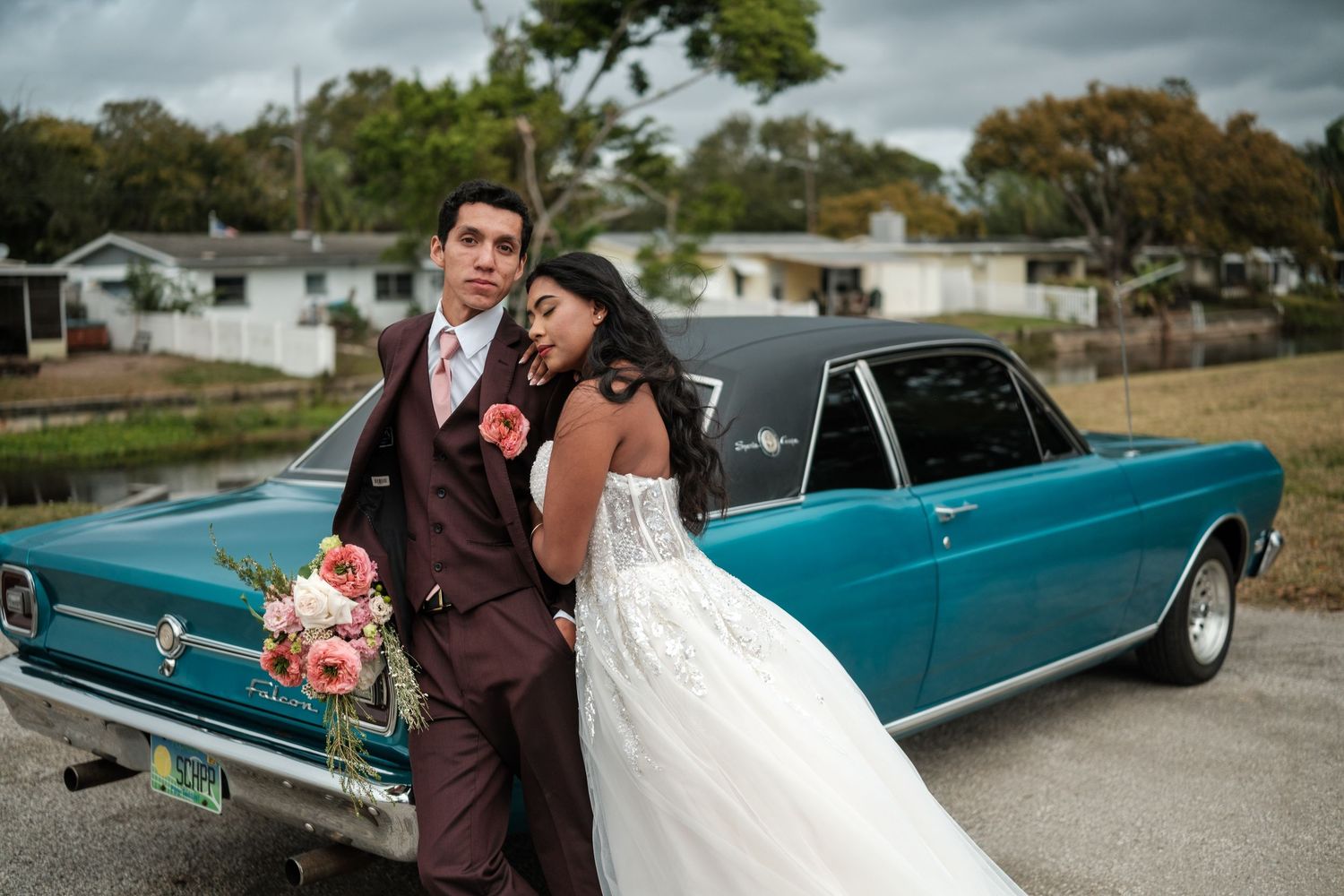 Newlyweds share intimate moments beside a retro turquoise automobile in an outdoor setting.