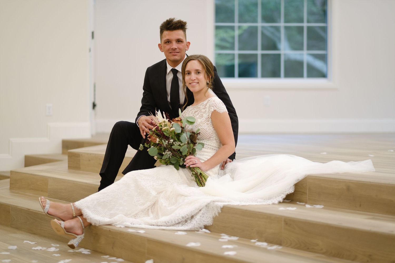 A wedding couple sits on white stairs during their photo session at an elegant venue.