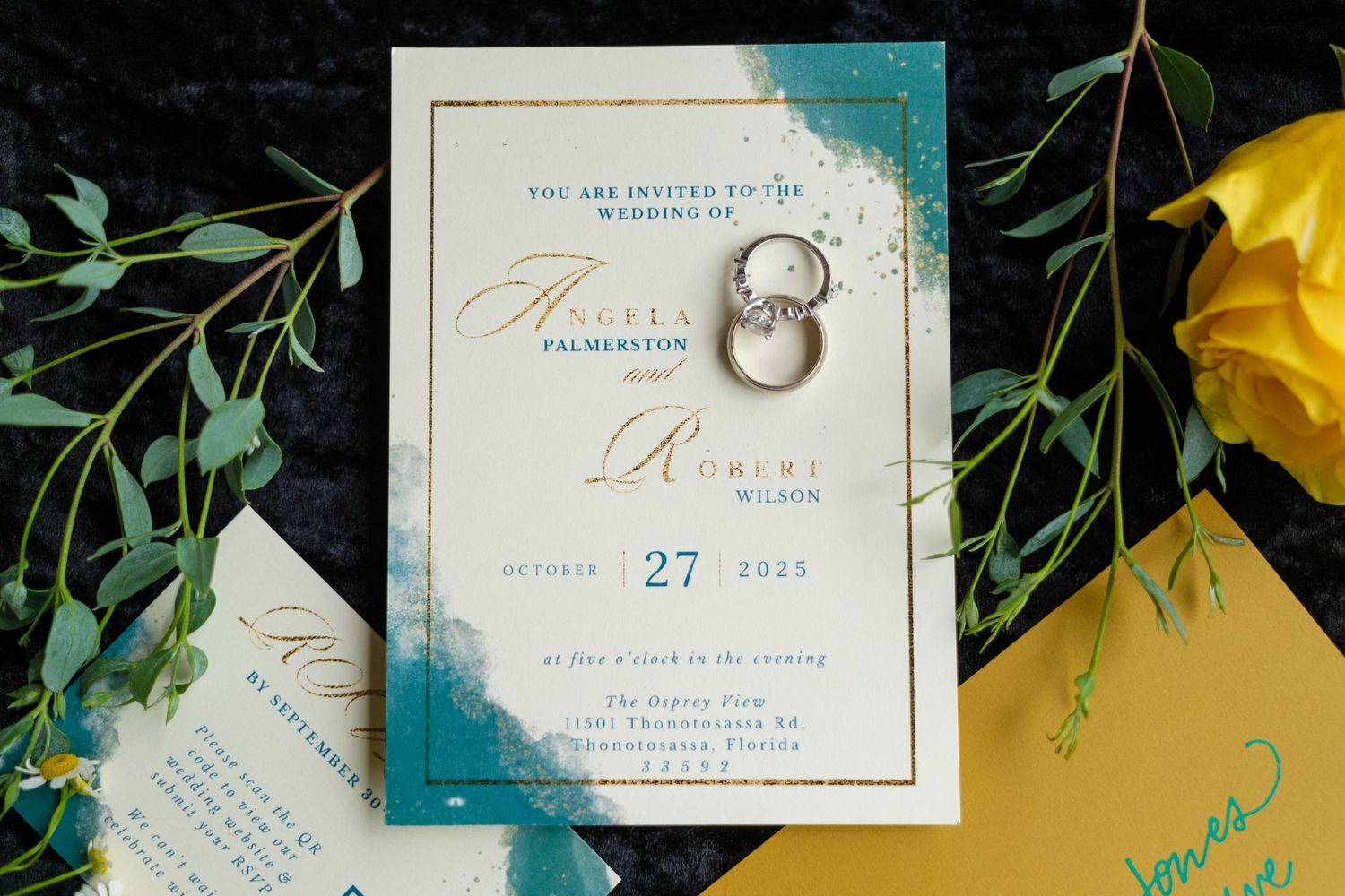 Wedding invitation suite with elegant gold calligraphy and greenery accents displayed on a dark background.