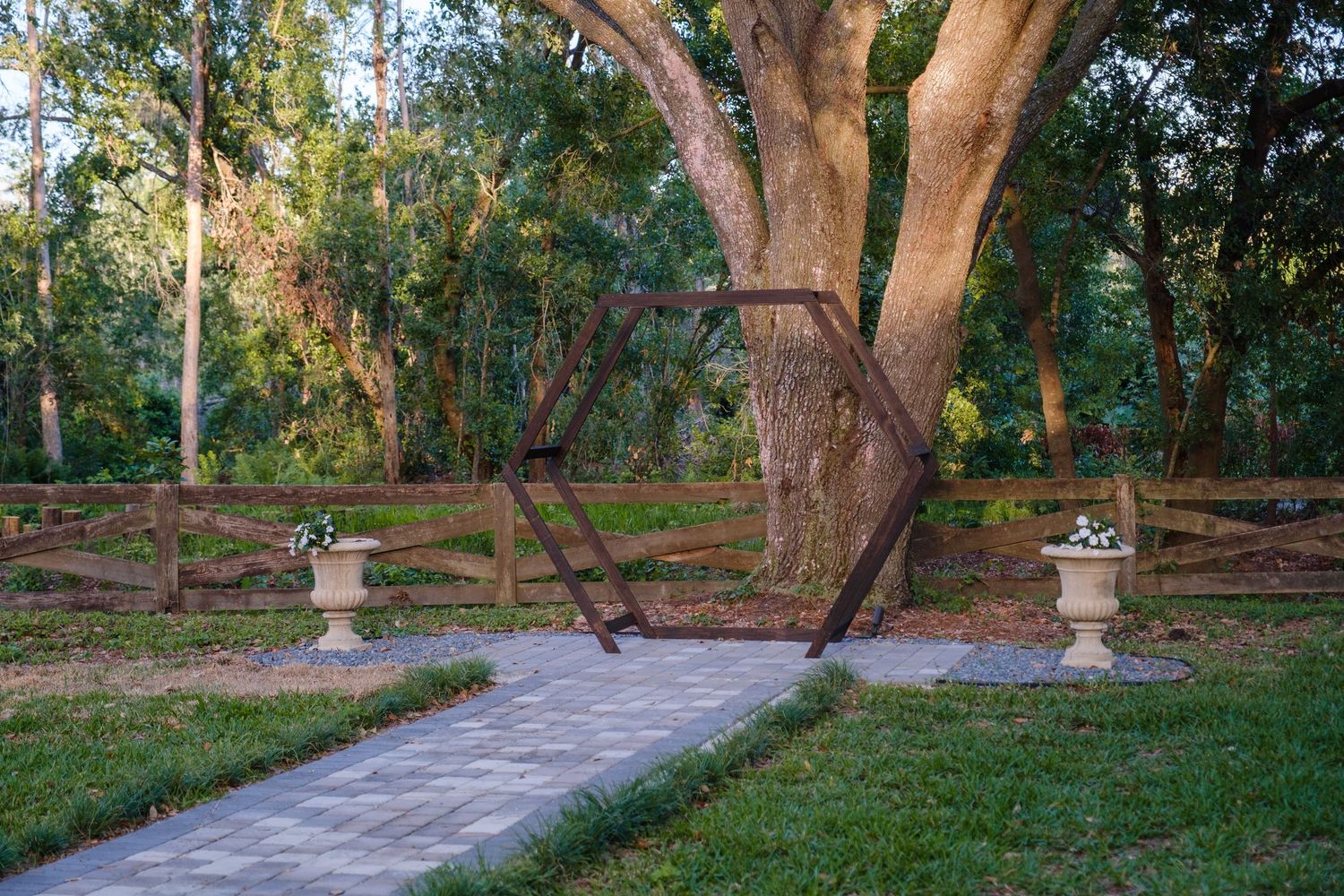A winding stone path leads through a tranquil garden with decorative urns and a majestic old tree.