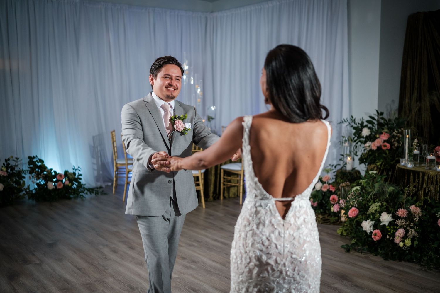 Wedding couple shares a first look moment in an elegant white-draped venue with floral decorations.