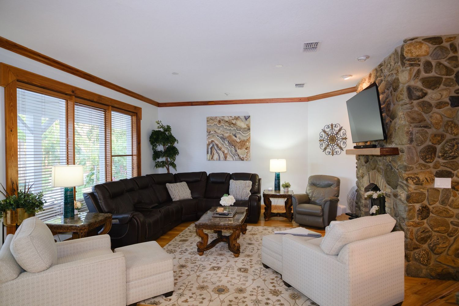 Luxurious living room with stone fireplace, plush sectional, white armchairs, and large windows letting in natural light.