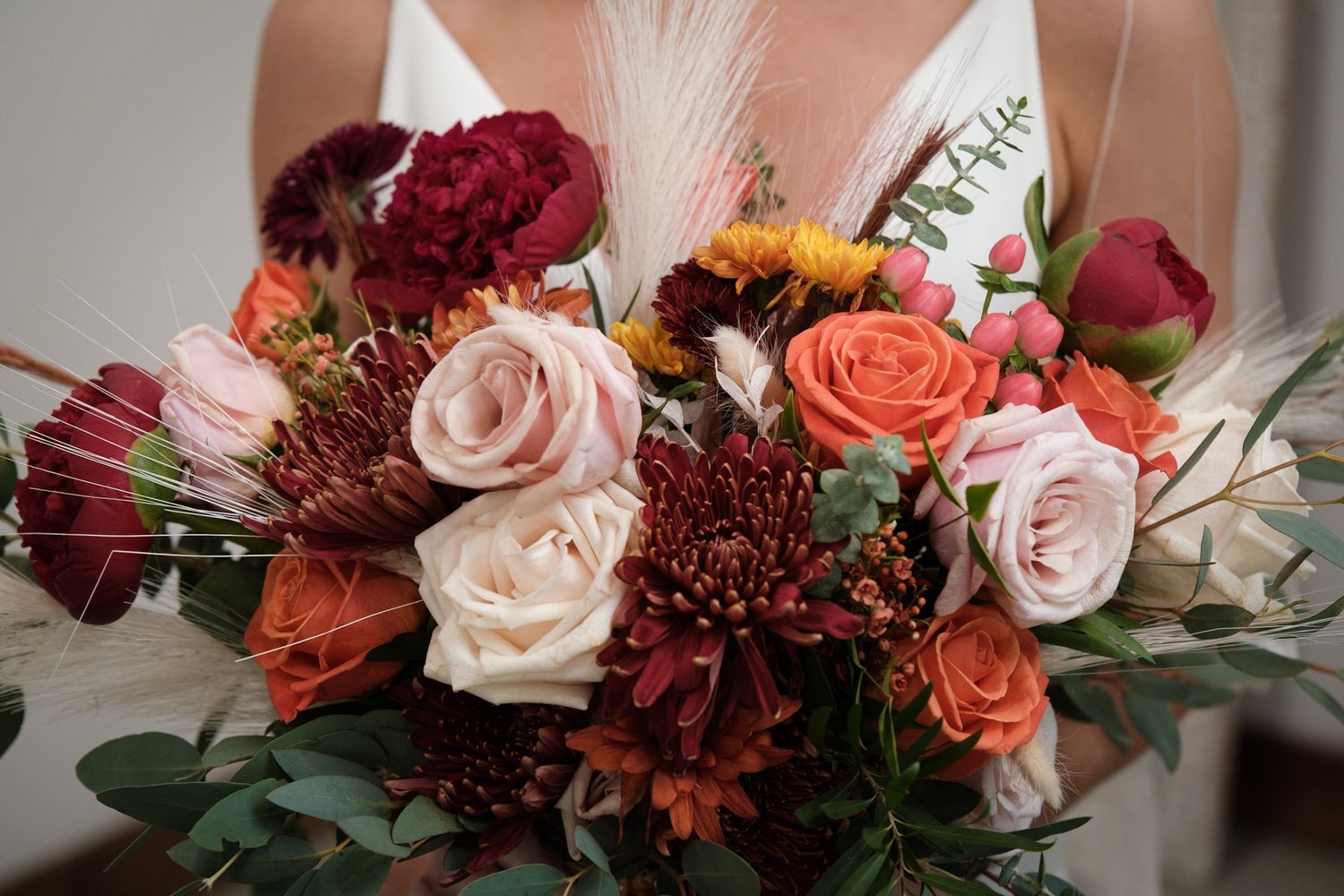 A romantic floral arrangement featuring roses, dahlias, and greenery in shades of coral, burgundy, and blush pink.