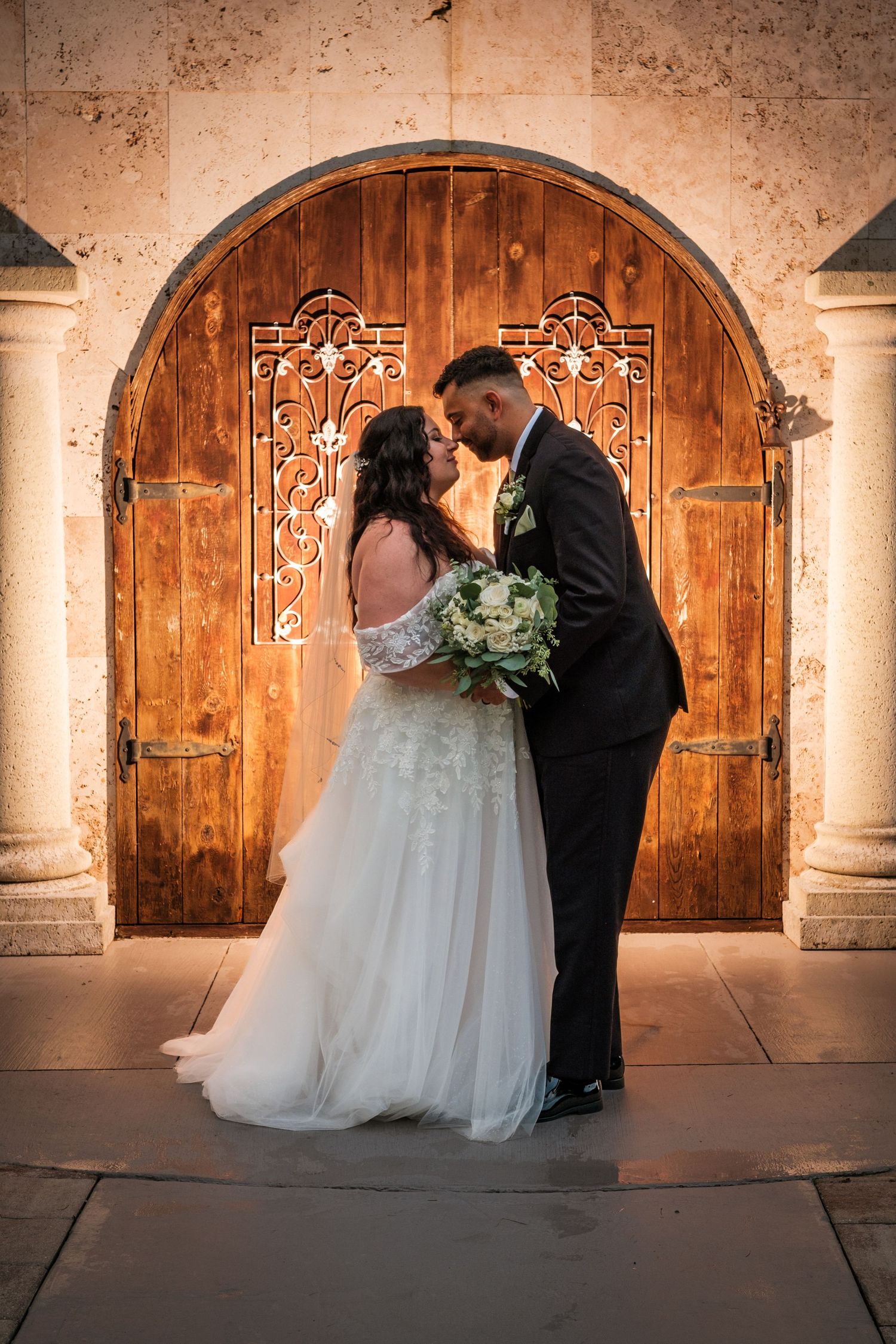A romantic wedding couple shares intimate moments in front of rustic wooden doors and stone columns.