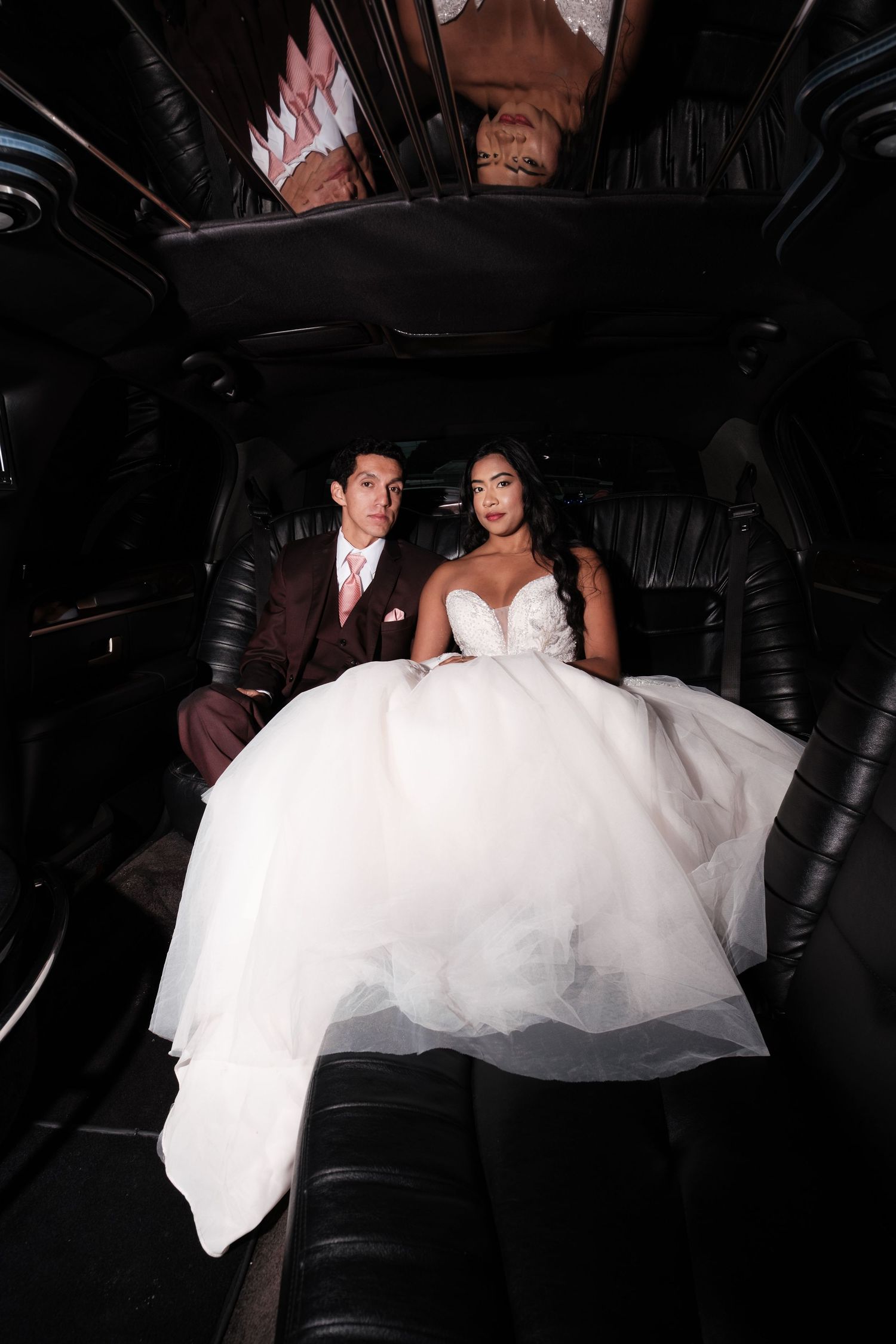 Wedding couple sitting in the dark interior of a limousine with flowing white dress.