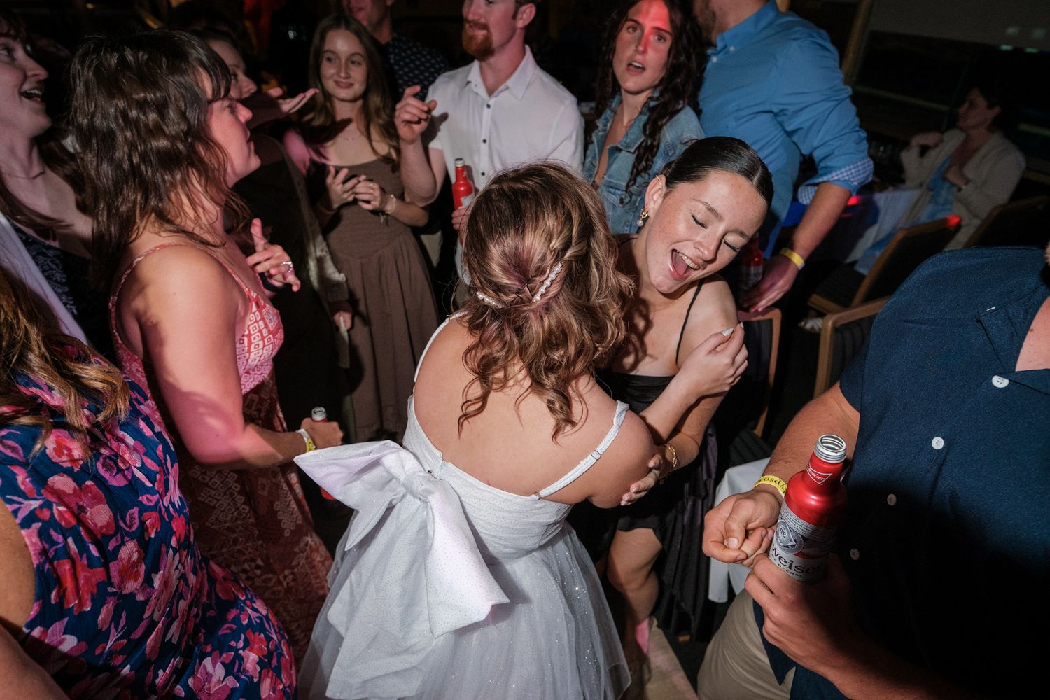 A lively crowd of people dancing and socializing at a dimly lit party or reception venue.