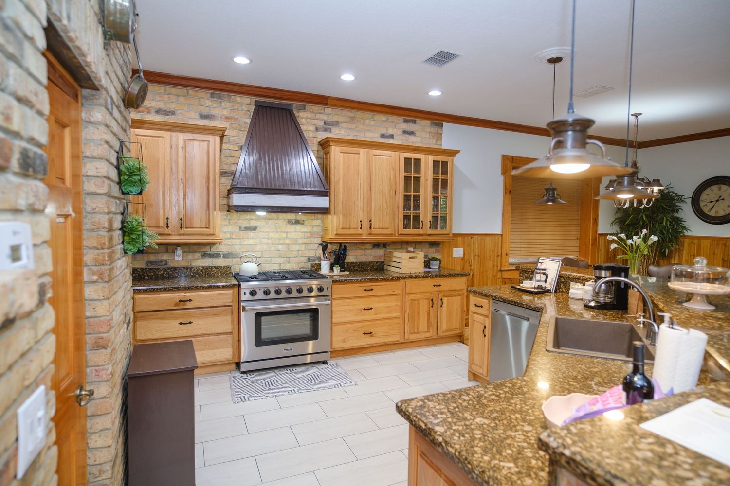 Modern kitchen with light wood cabinets, granite countertops, stainless appliances and stone accent wall features.