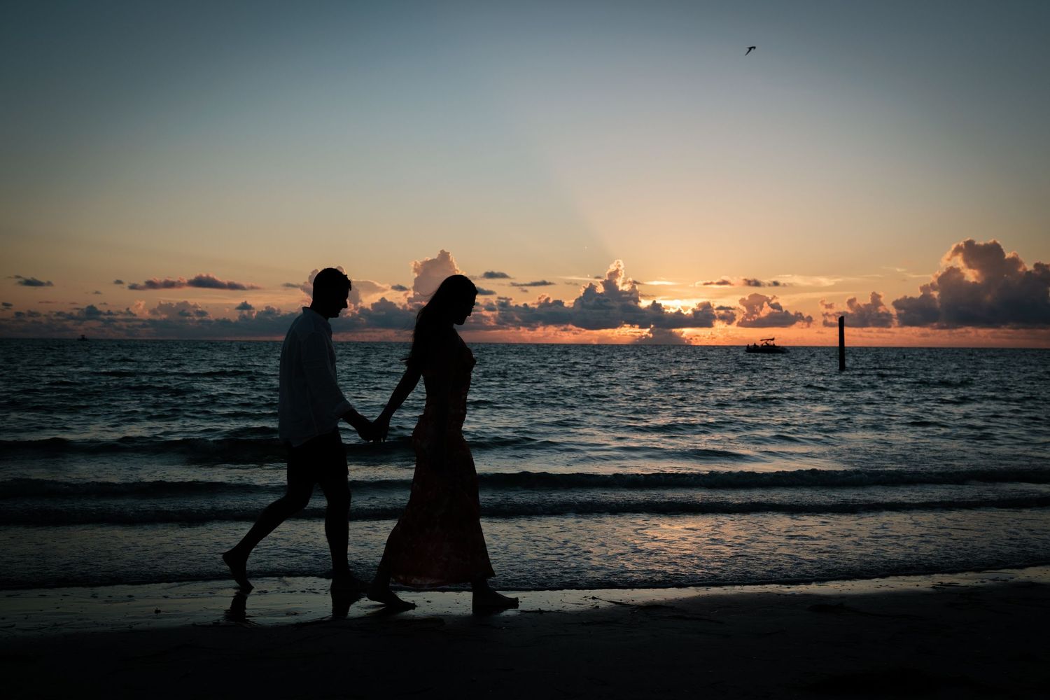 Silhouetted figures walk along a beach at sunset with dramatic orange and purple sky over the ocean.