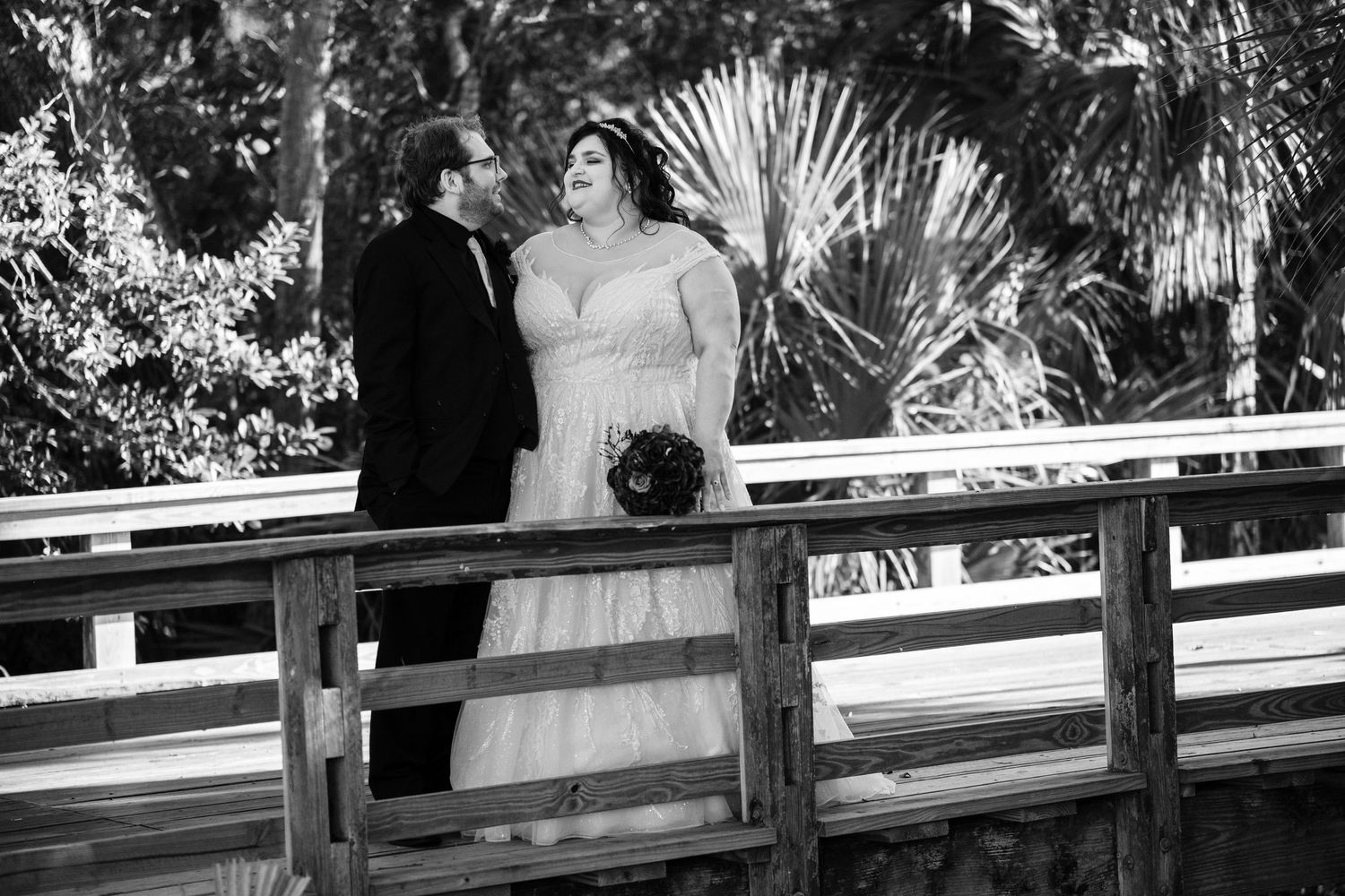 Wedding ceremony guests seated in white chairs on a lawn with palm trees and greenery in the background.