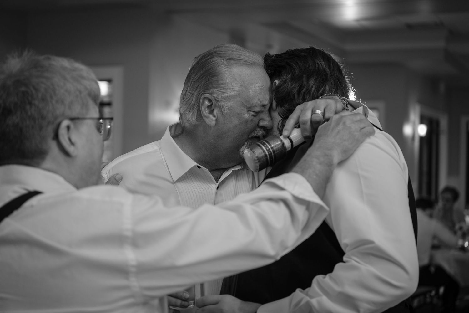 Black and white photo of two men sharing an emotional hug at a wedding reception.