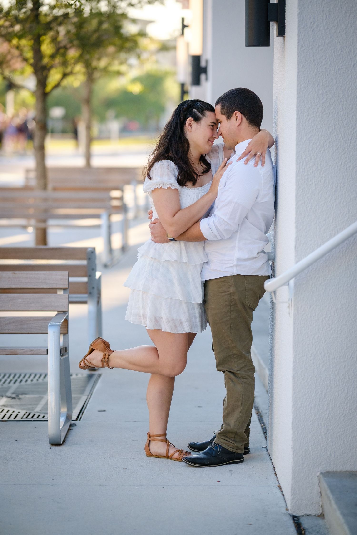 Romantic couple in white outfits sharing a close moment leaning against a white building outdoors.