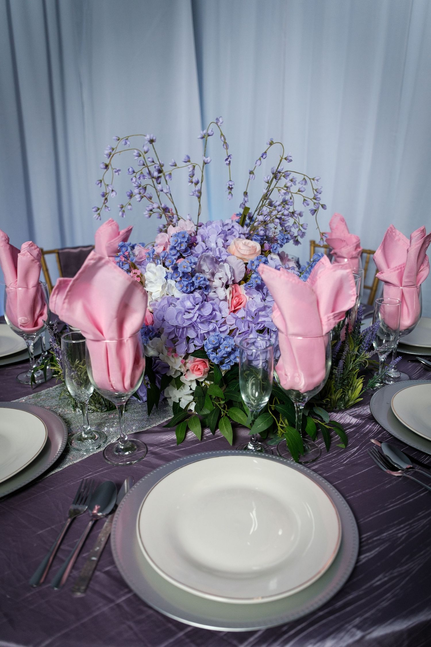 Wedding table setting with pink tulips and purple flowers on dark tablecloth with white plates.