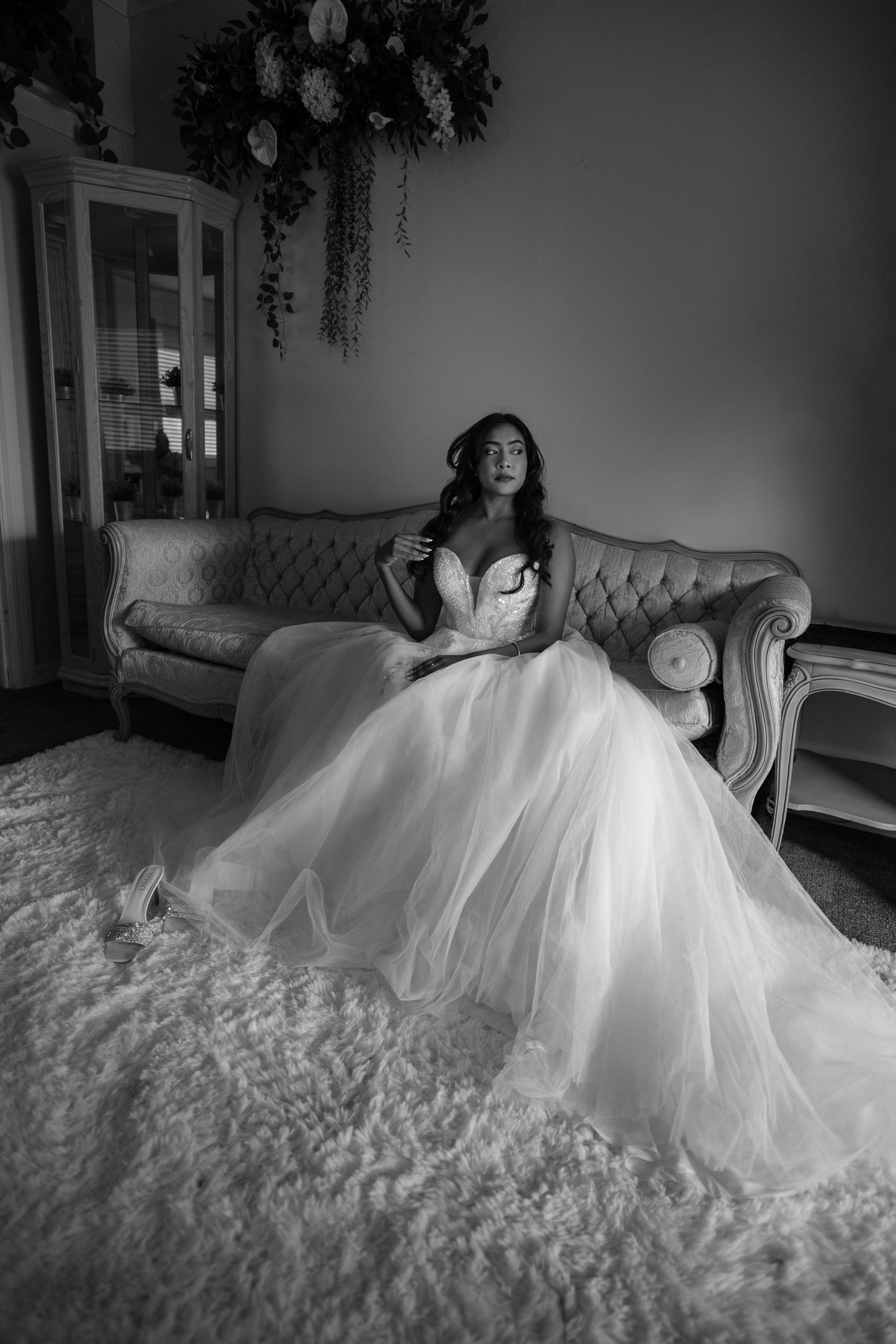 A bride in a flowing white wedding gown reclines elegantly on a vintage sofa in a romantic indoor setting.