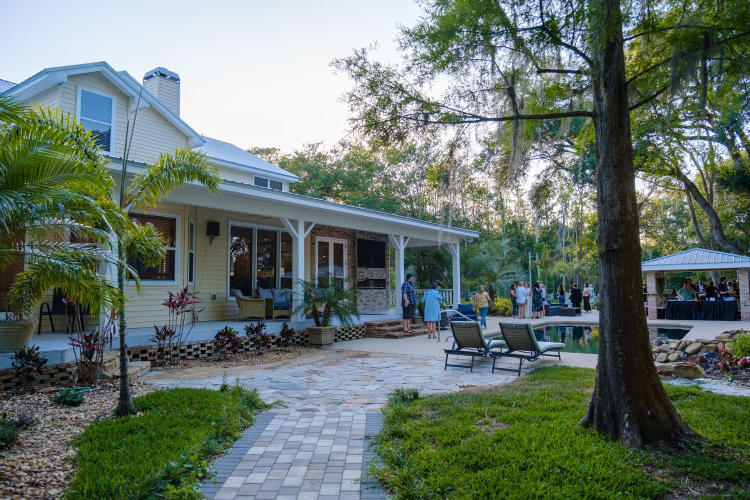 A charming southern-style house with a porch and landscaped pathway featuring palm trees and paved walkways.