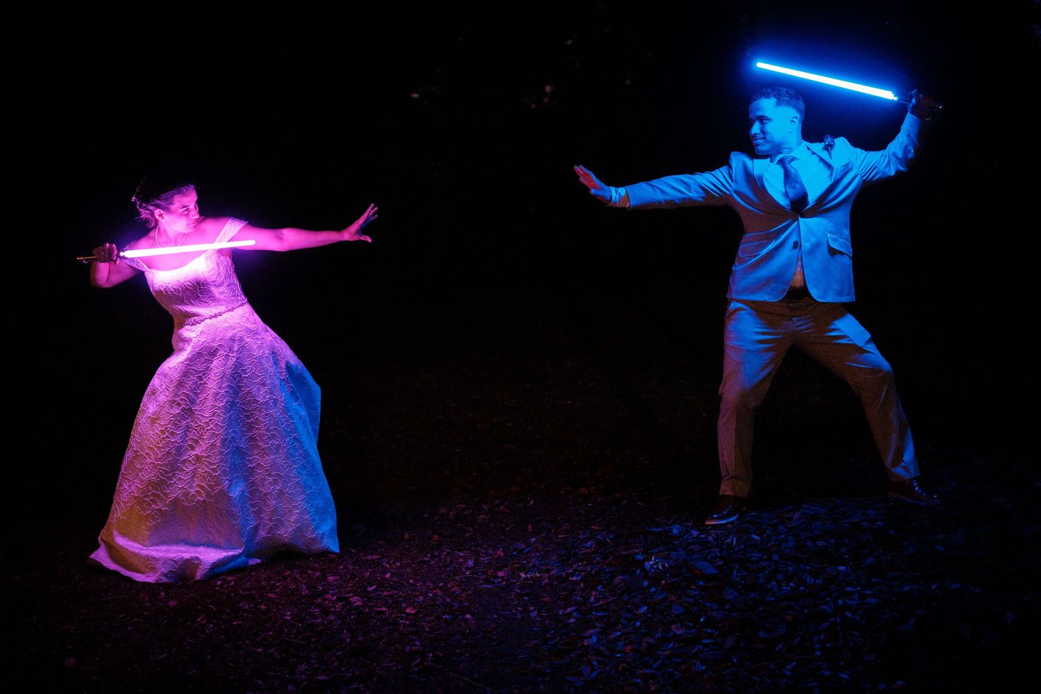 Bride and groom wielding glowing lightsabers in a Star Wars-themed wedding photo shoot at night.