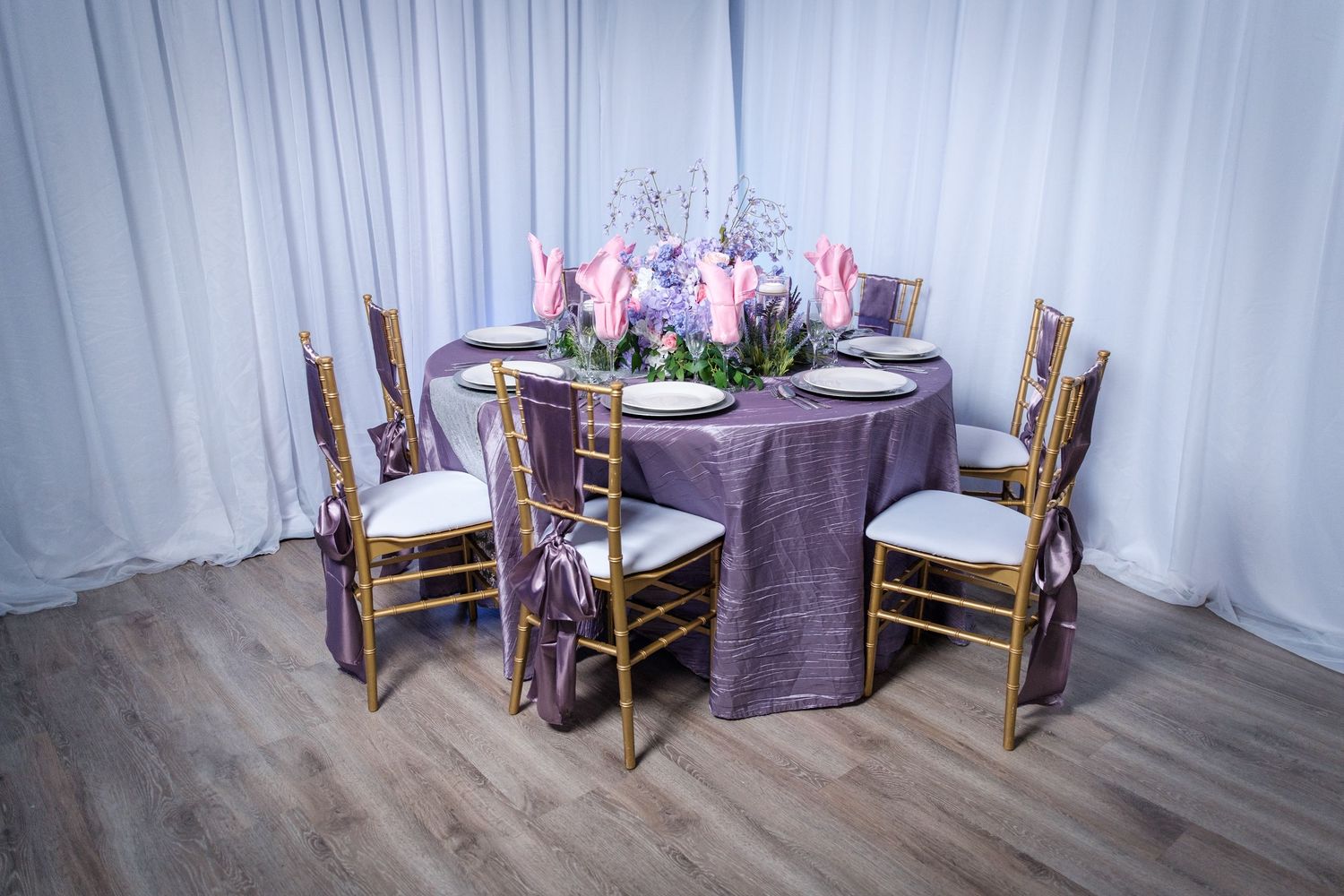 Round dining table with purple tablecloth and gold chiavari chairs decorated with pink tulip centerpiece.